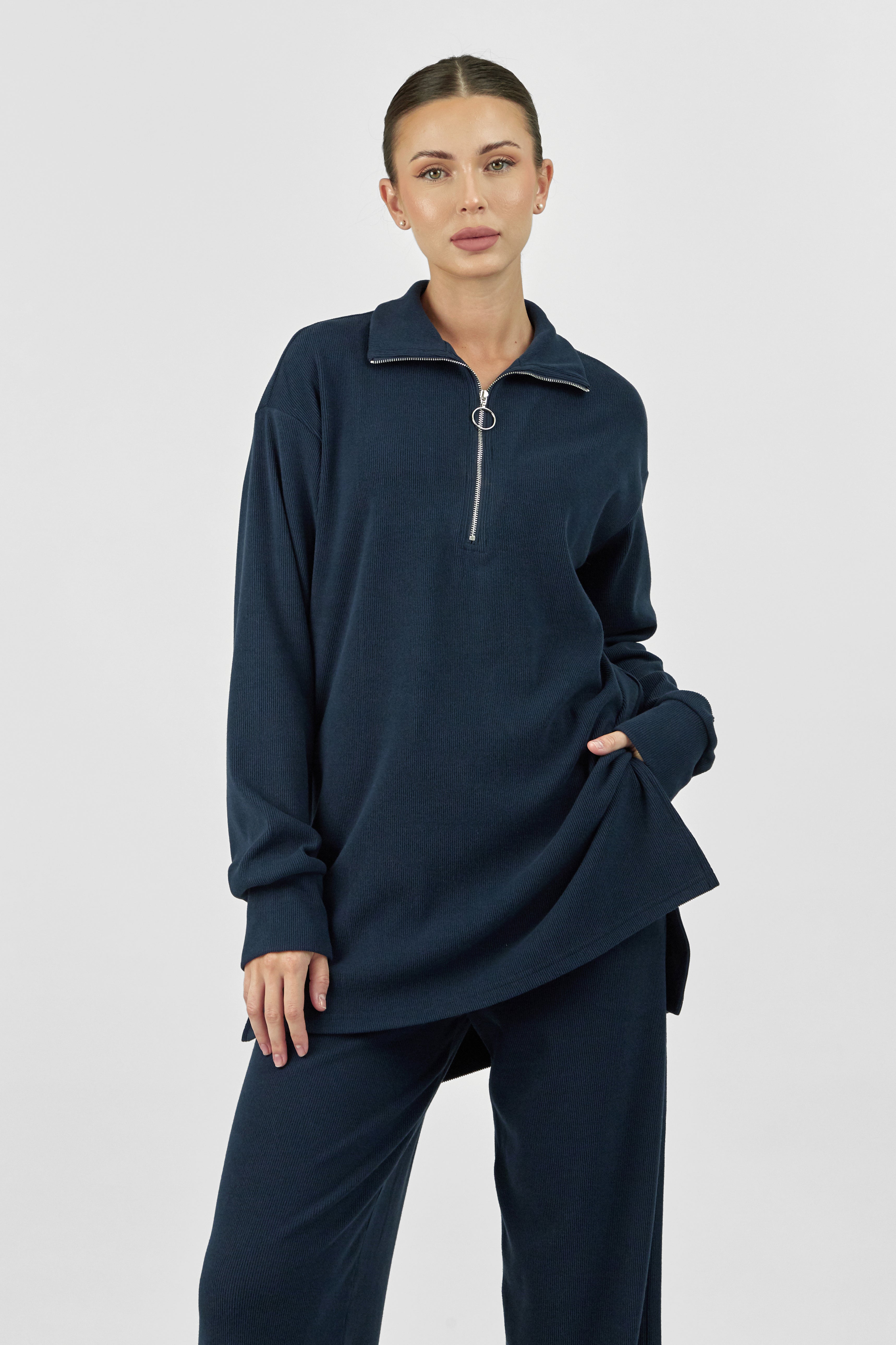 A closer look of a girl is wearing FARES' velour knit half zip. She is standing with her left hand in her pocket. Colour description: Navy Blue.