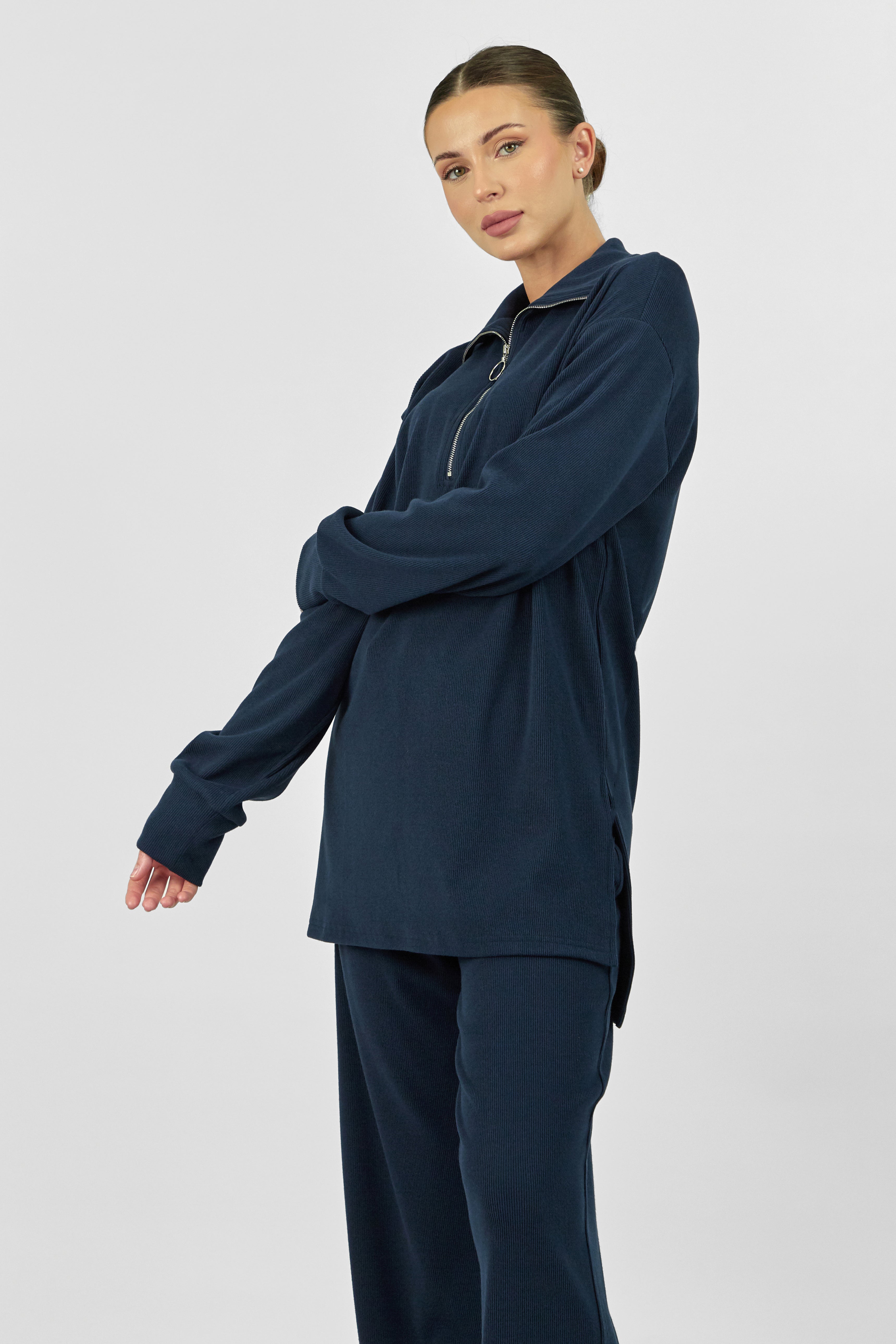 A model is wearing FARES' velour knit half zip with her left hand crossing her body. Colour description: Navy Blue.