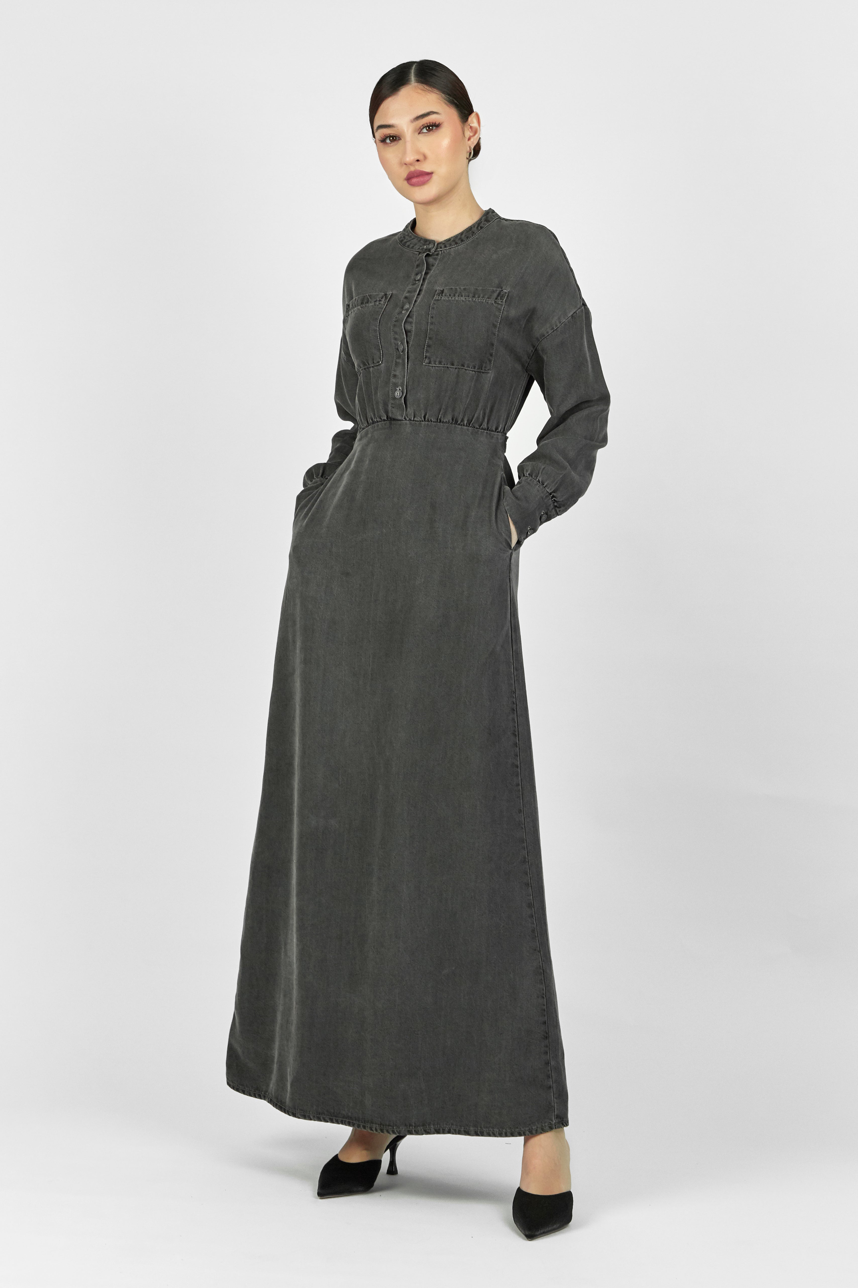 A model is wearing FARES' soft touch denim style dress while facing the camera and her hands are in her pocket. Colour description: Dark Grey.
