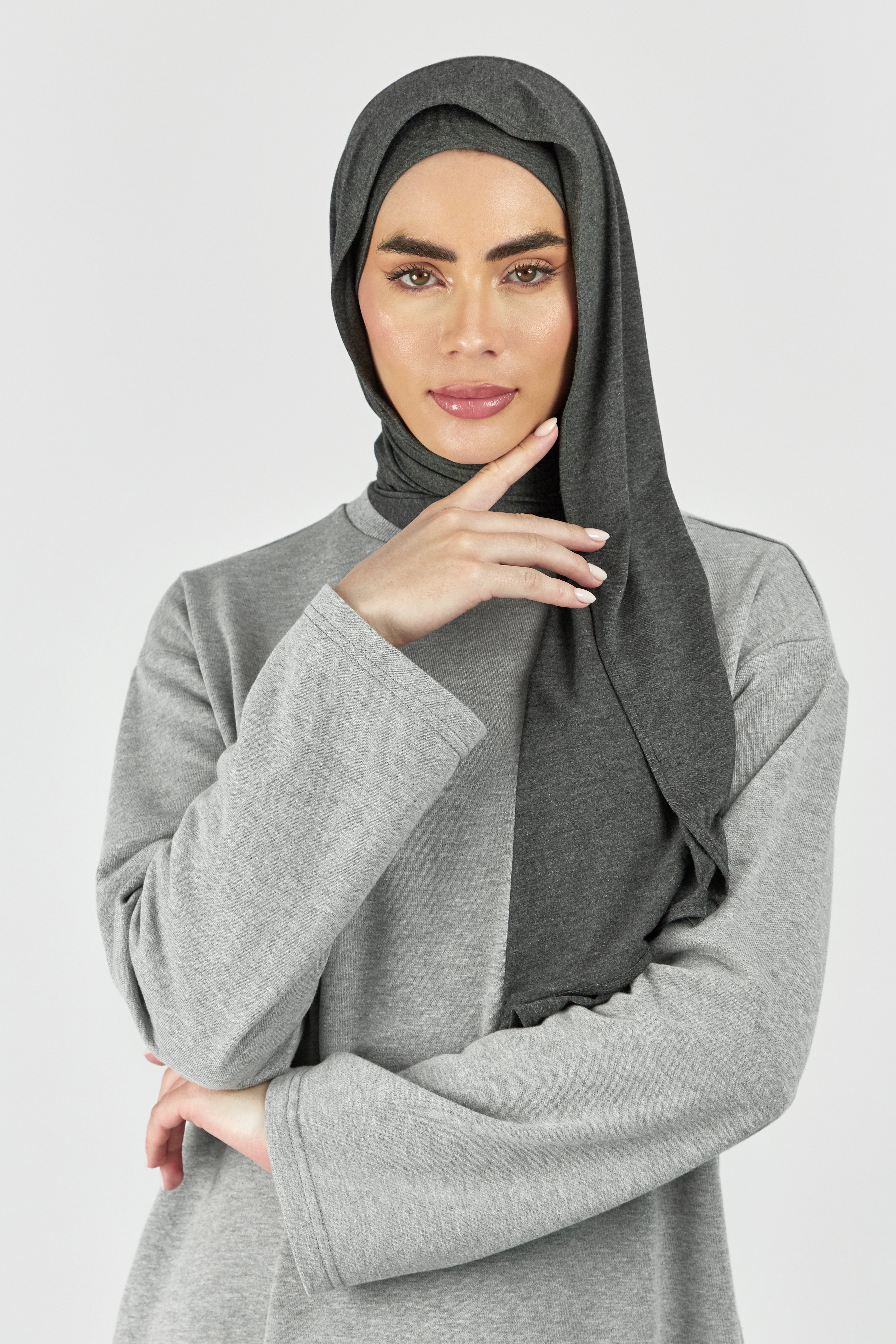A woman wearing one of FARES's matching jersey hijab sets. This set includes a modal jersey hijab and matching undercap. Colour description: dark heather grey.