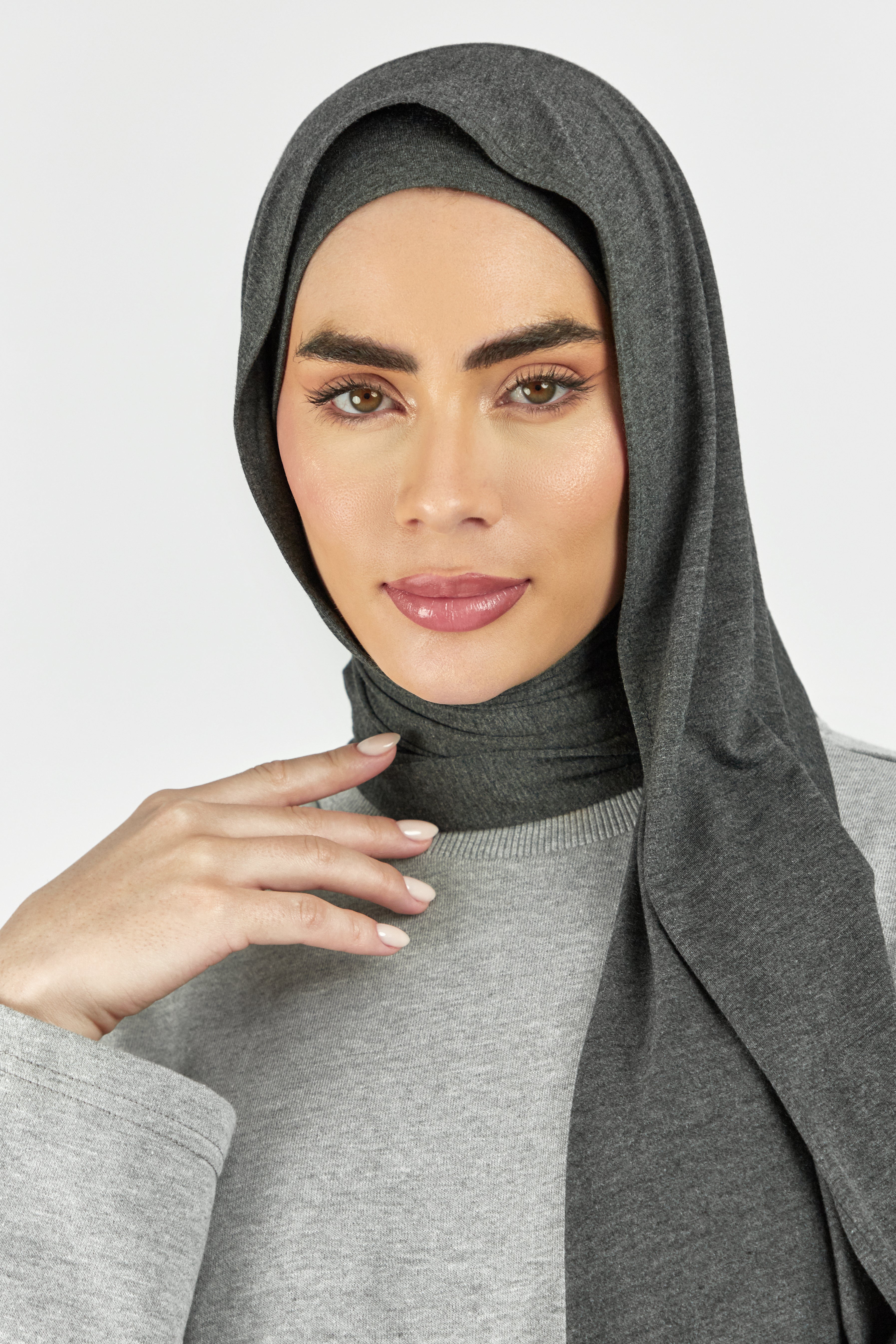 A close-up of a woman wearing one of FARES's matching jersey hijab sets. This set includes a modal jersey hijab and matching undercap. Colour description: dark heather grey.