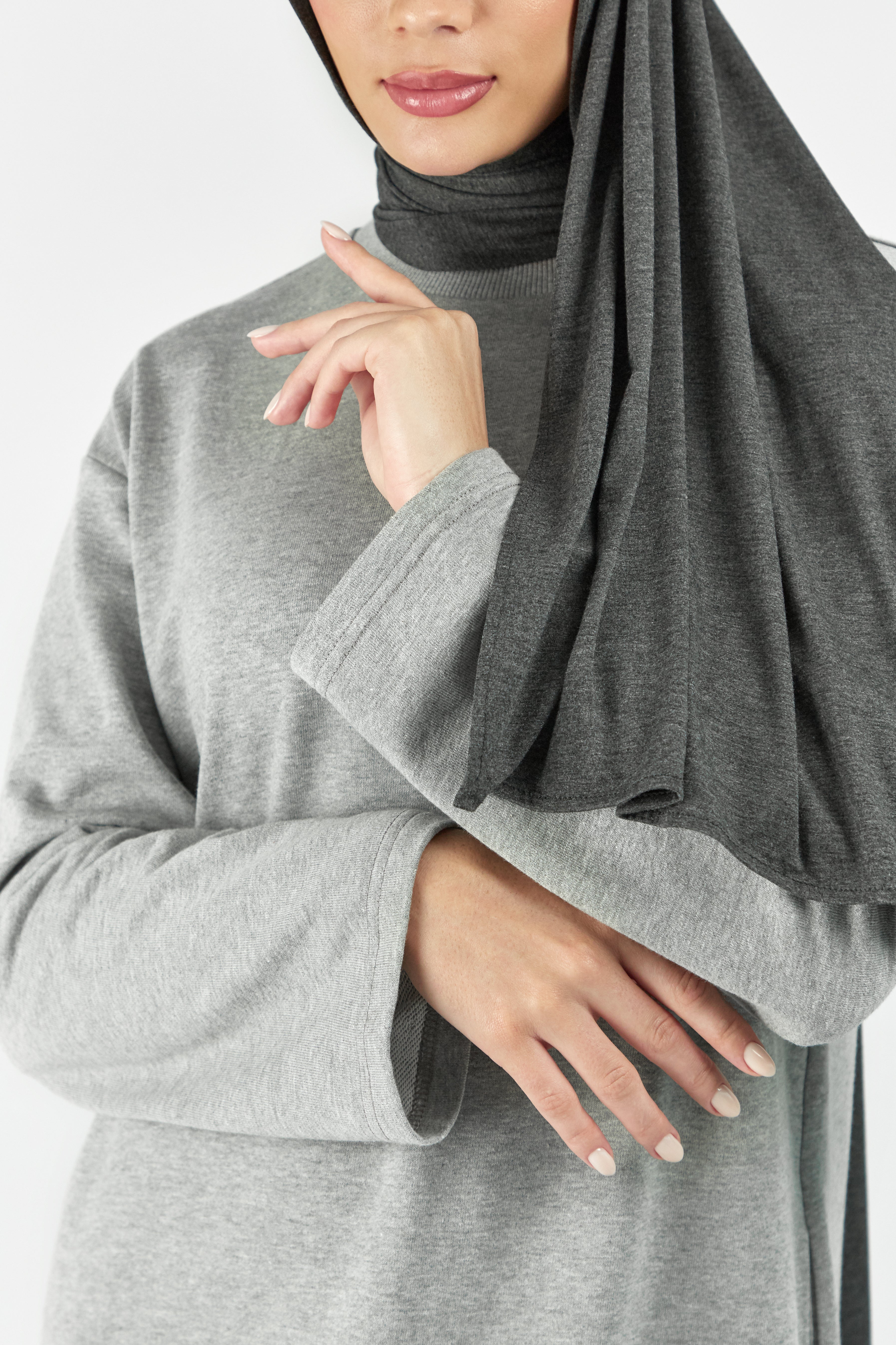 A close-up of the front of a female model wearing one of FARES's matching jersey hijab sets. Colour description: dark heather grey. This set includes a modal jersey hijab and matching undercap.