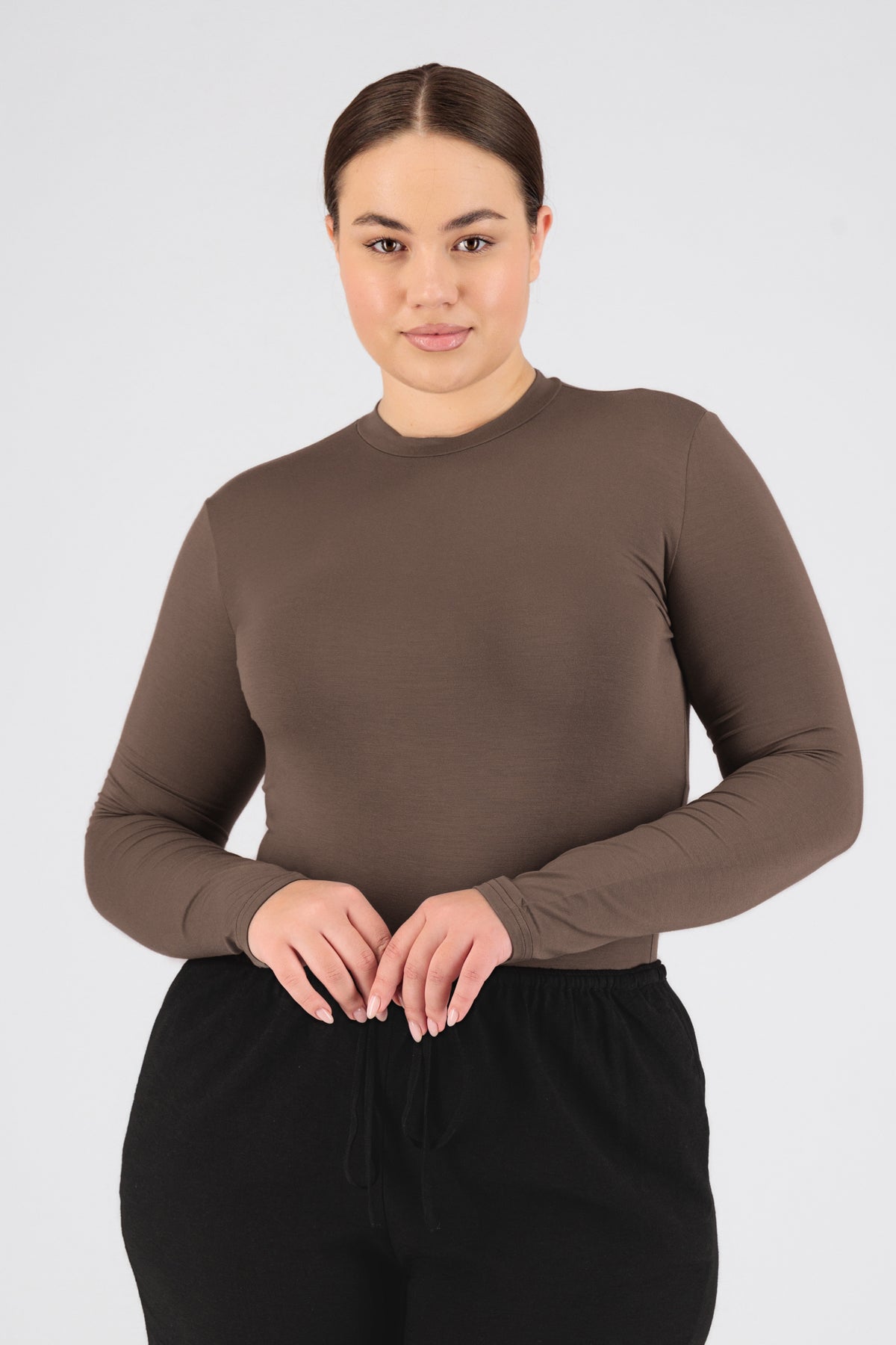 The model is wearing FARES' long sleeve layer. Colour description: Cold Brown. She is facing the camera in a base layer with her hands in her hips.