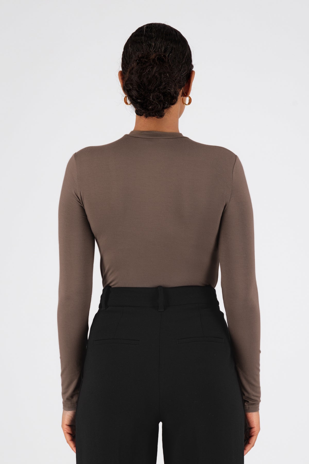 A model wearing FARES' long sleeve layer is shown from the back facing the wall. Colour description: Cold Brown.