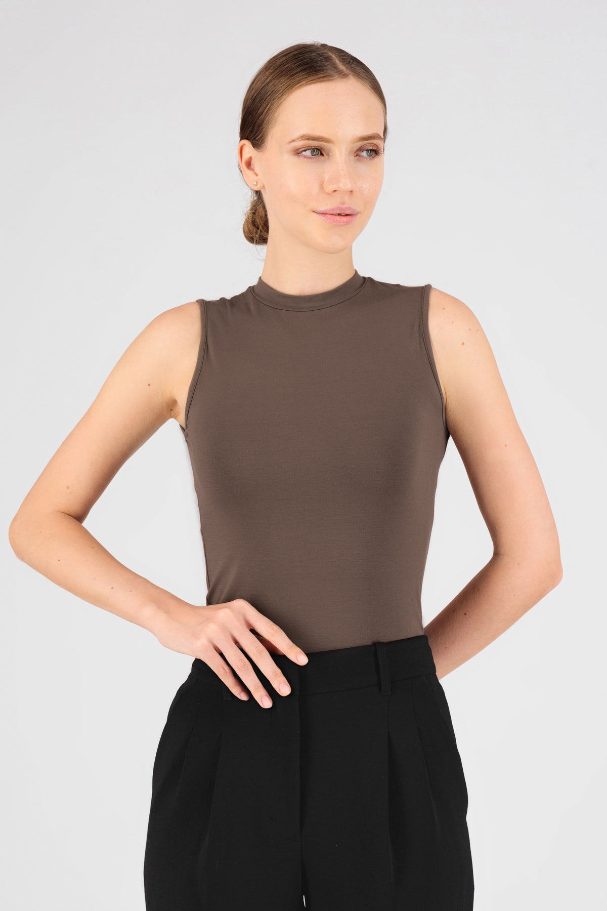 A model is wearing FARES' sleeveless layer. She is standing in the sleeveless top while looking to the right. Colour description: Ash Brown.