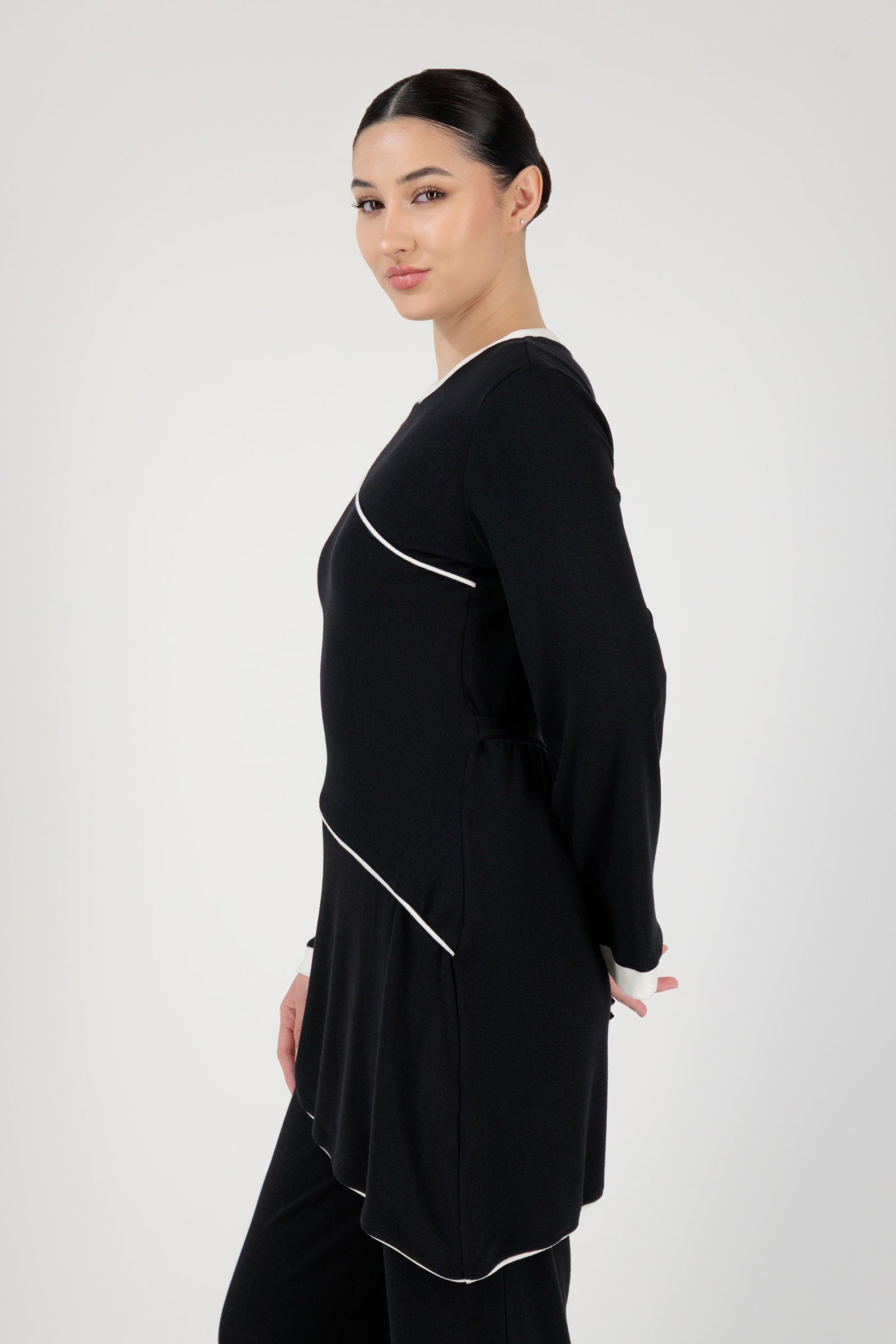 Side angle of the FARES Slanted Contrast Detail Knit Tunic in Black presenting an elegant tunic shape defined by slanted contrast accents.