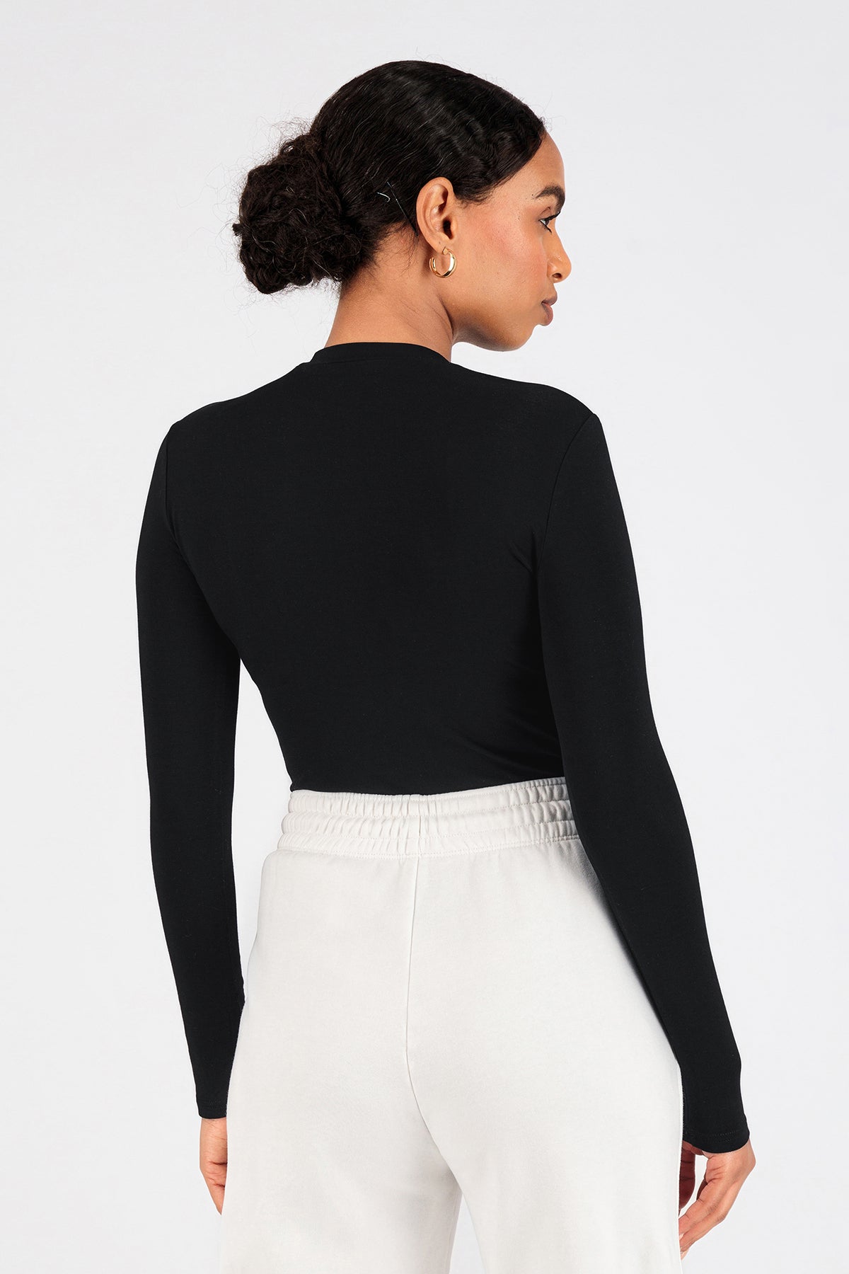 A model wearing FARES' long sleeve layer is shown from the back while her head is turned to the right. Colour description: Black.