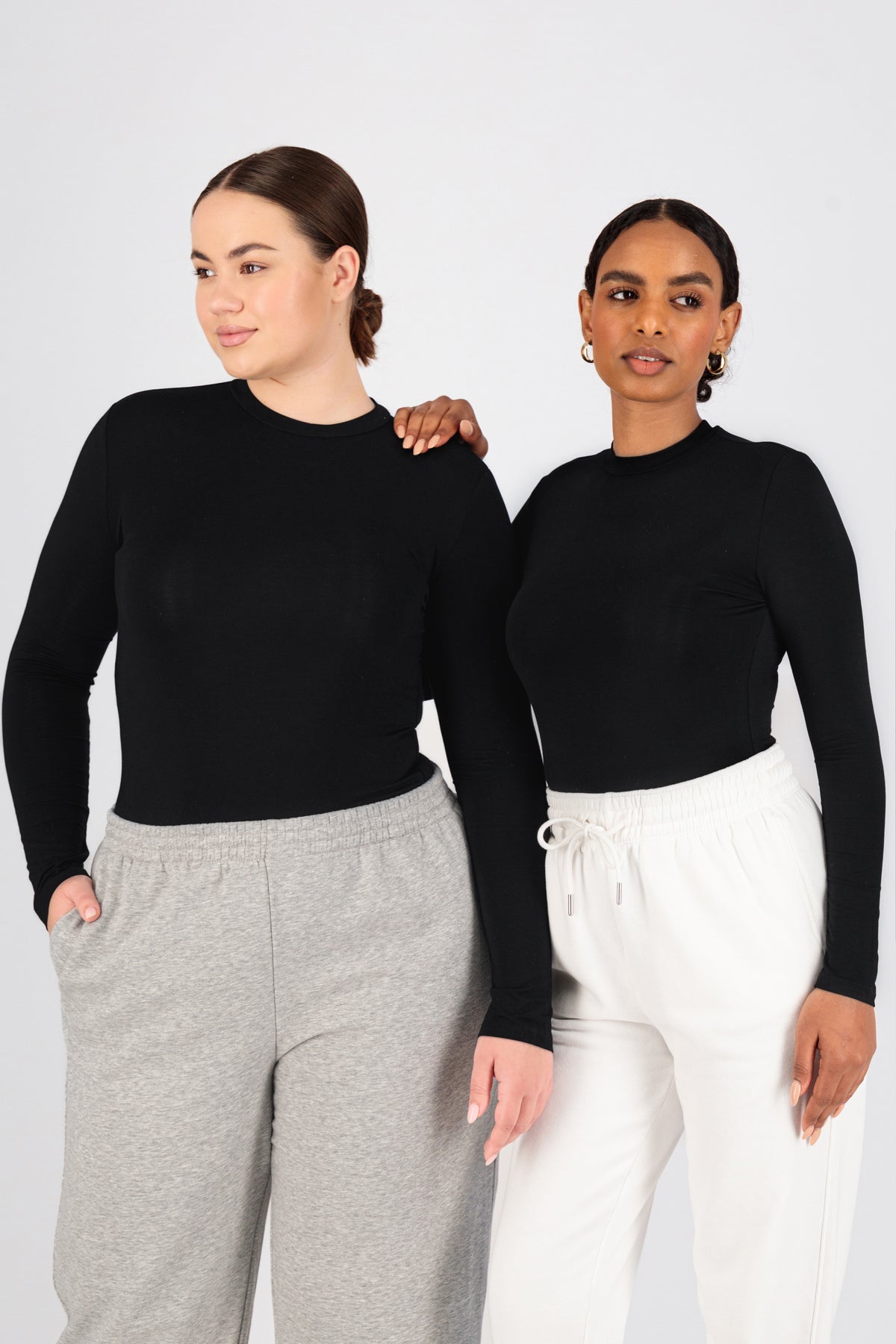 Two girls are standing side by side in FARES' best base layer clothing. Colour description: Black. One of the girls is resting her hand on the other girl's shoulder.