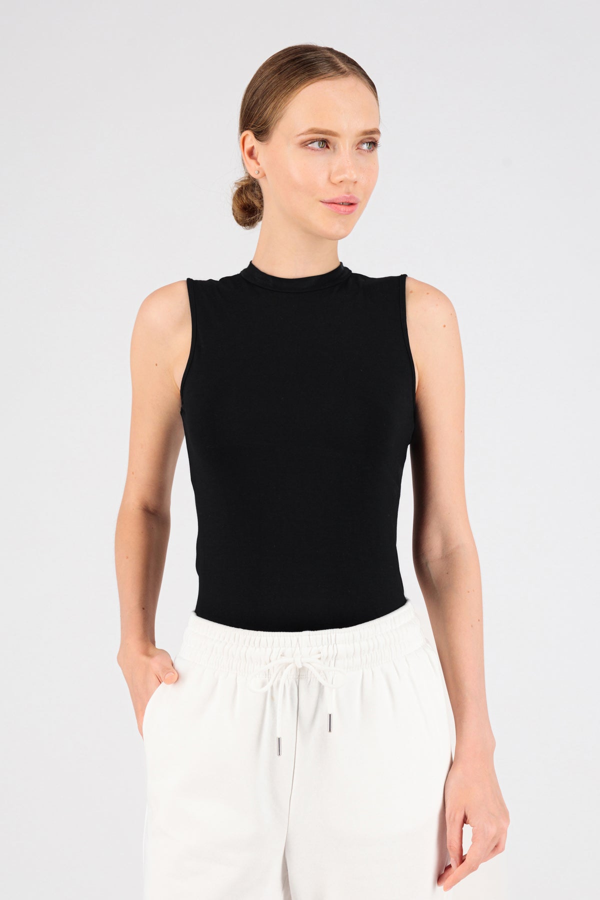 The girl is wearing FARES' sleeveless layer. Colour description: Black. She is standing in the sleeveless top while looking to the right.
