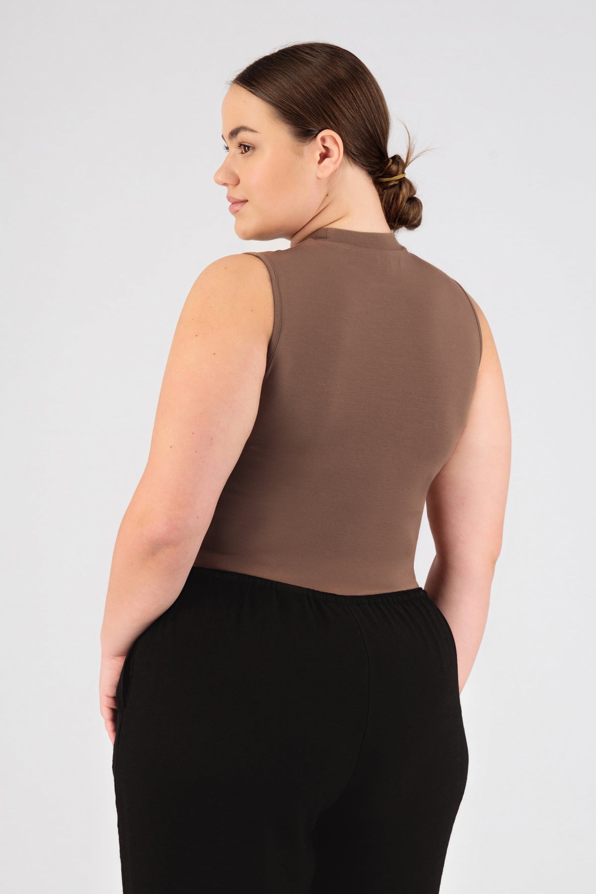 A girl wearing FARES' sleeveless layer is shown from the back while looking over her left shoulder. Colour description: Bronze.