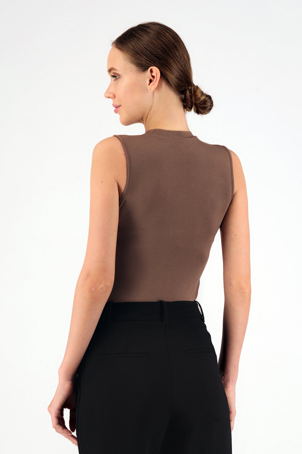 Colour description: Bronze. A model wearing FARES' sleeveless layer is standing with her back while looking over her left shoulder.
