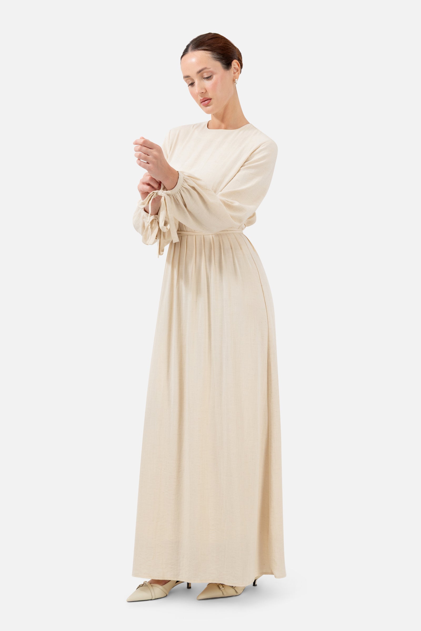 Woman standing in the Crema Tie Detail Darted Waist Dress with long sleeves and a graceful silhouette.