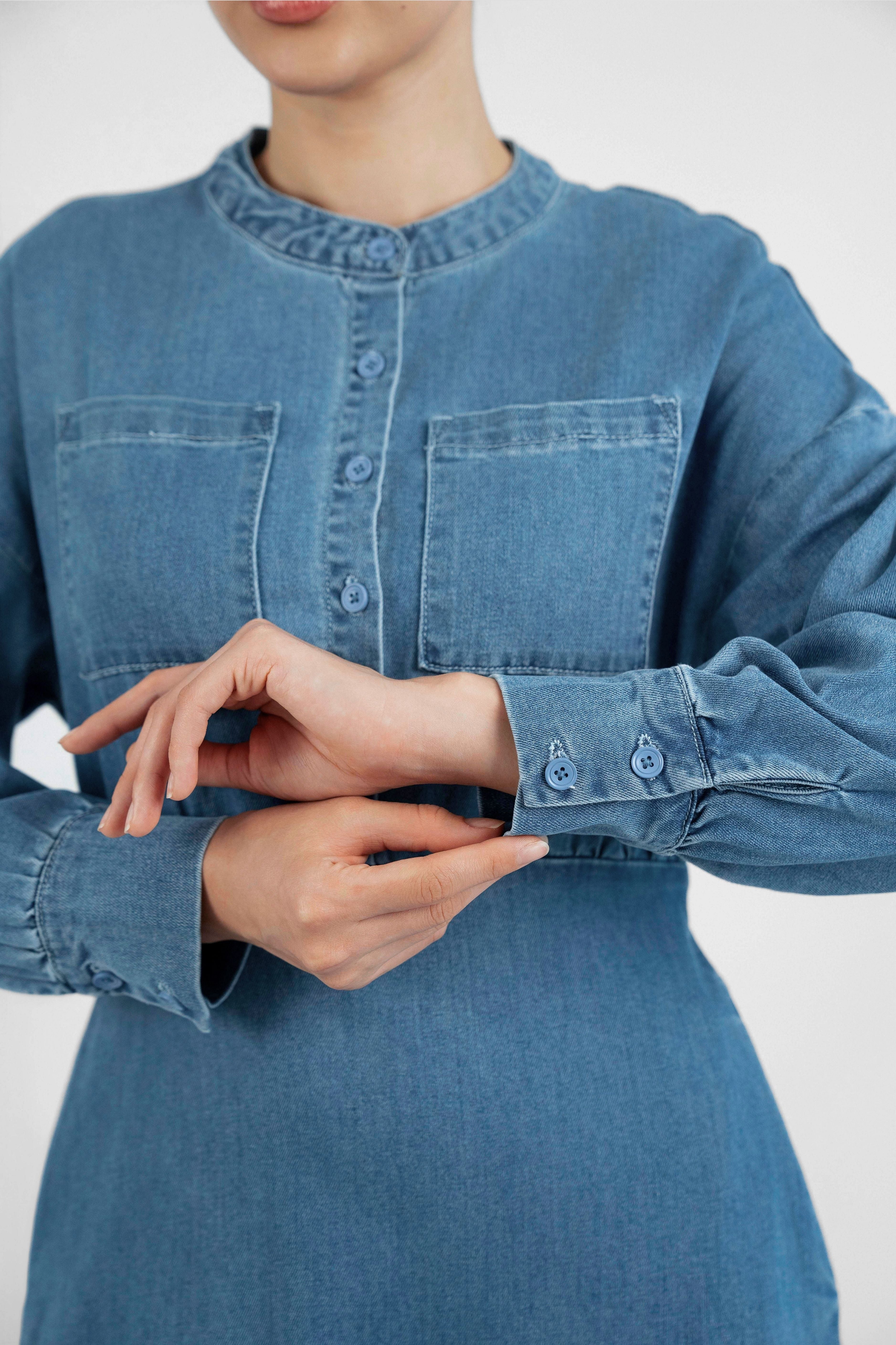 A close up of a girl wearing FARES' denim dress while showcasing the sleeves of the dress. Colour description: Blue.