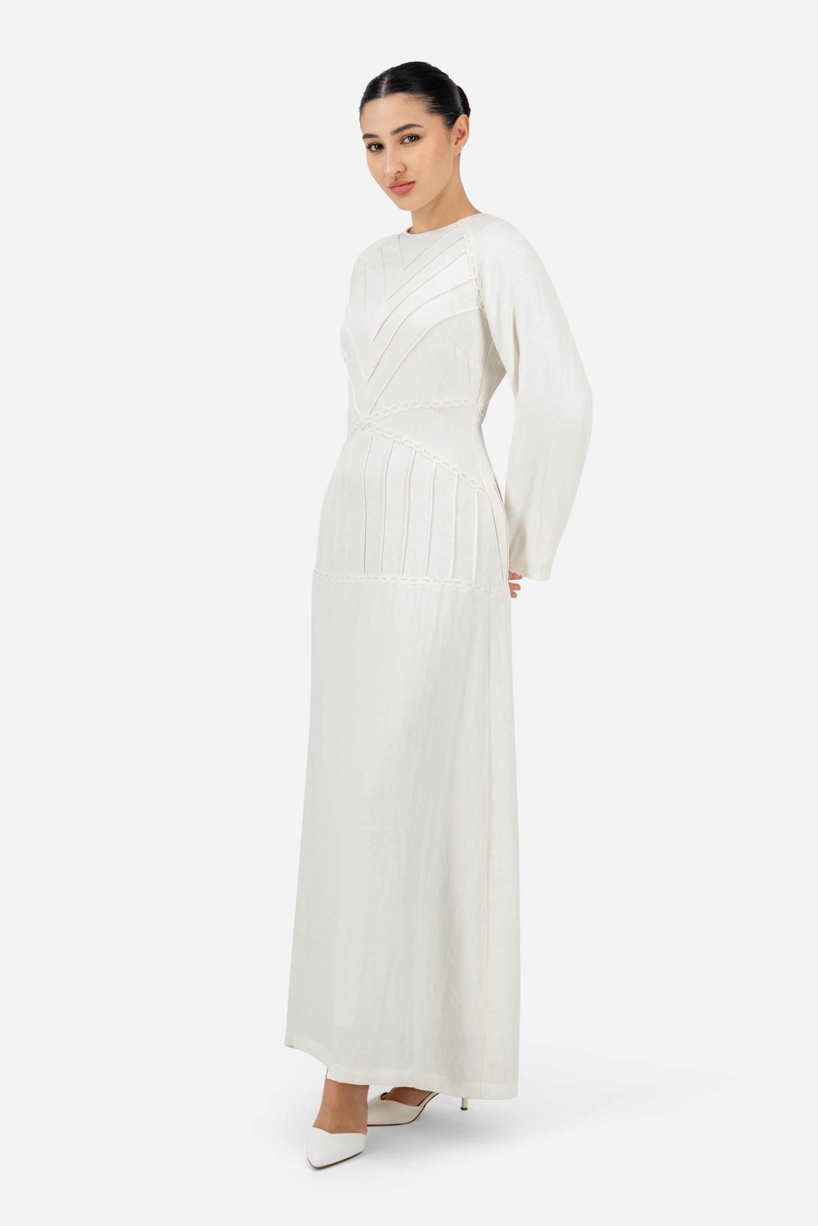 Woman standing in the White Ivory geometric detail maxi dress with long sleeves.
