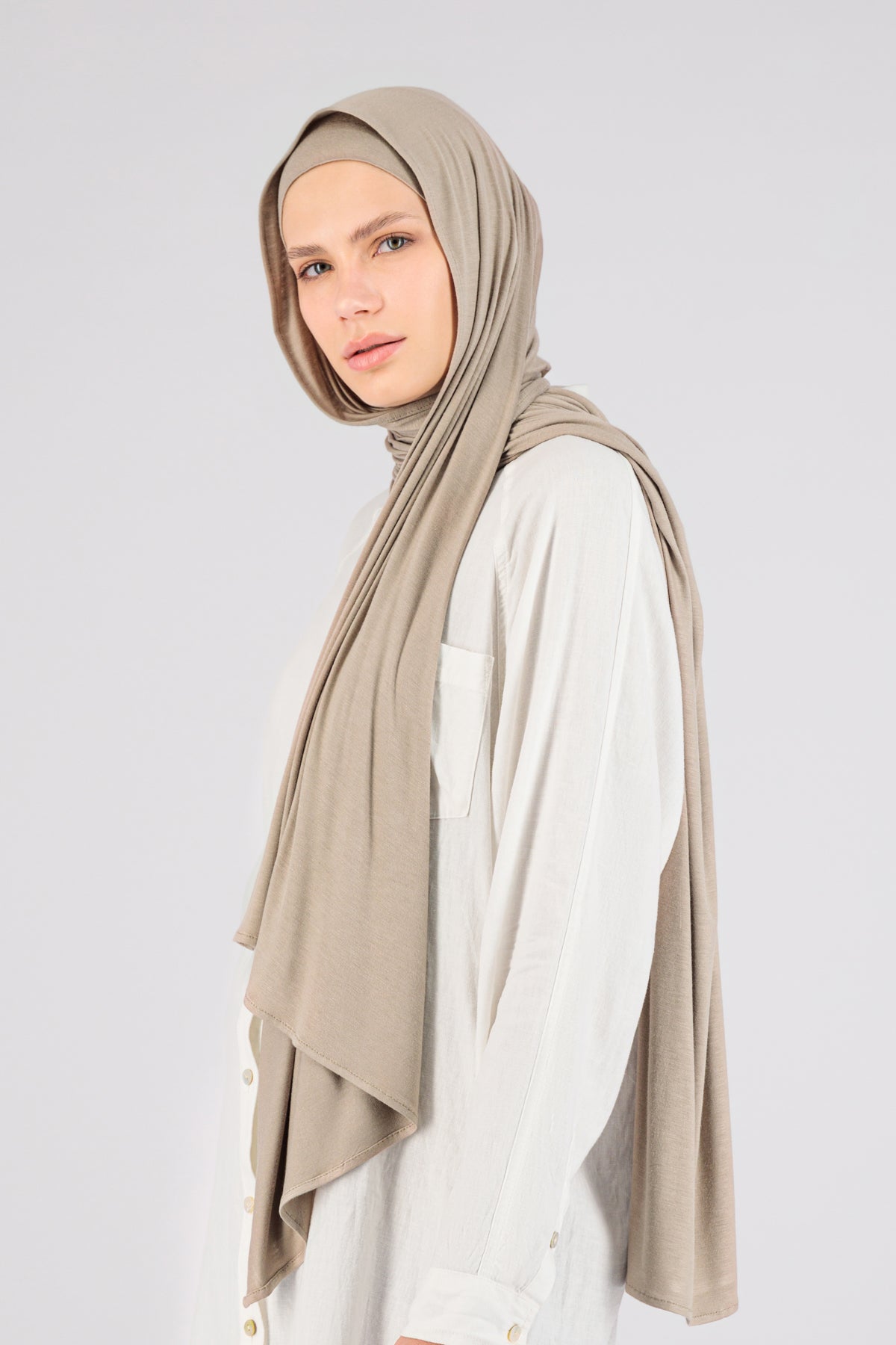 A woman wearing one of FARES's matching jersey hijab sets. The model is turned to the left. Colour description: light beige. This set includes a modal jersey hijab and matching undercap.