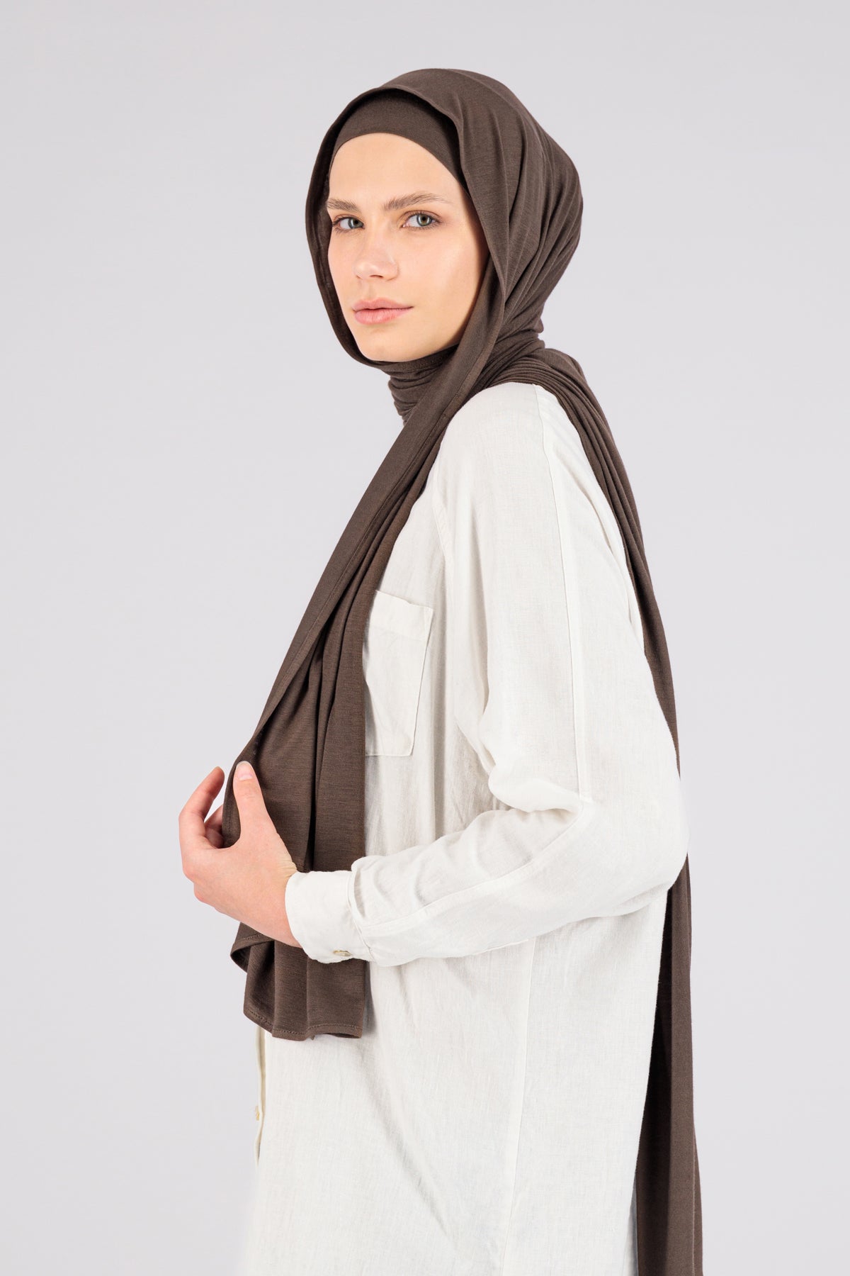 A woman wearing one of FARES's matching jersey hijab sets. The model is turned to the left. Colour description: cool dark brown.
