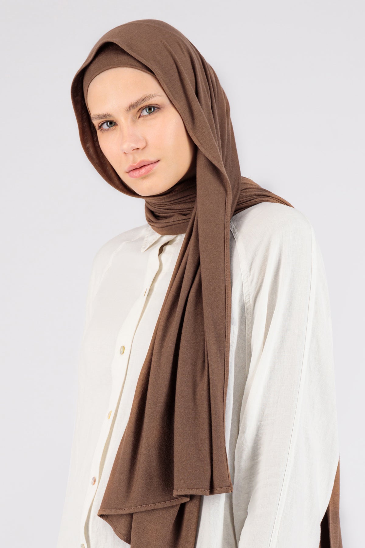 A woman wearing one of FARES's matching jersey hijab sets. The model is turned to the left. Colour description: warm brown.