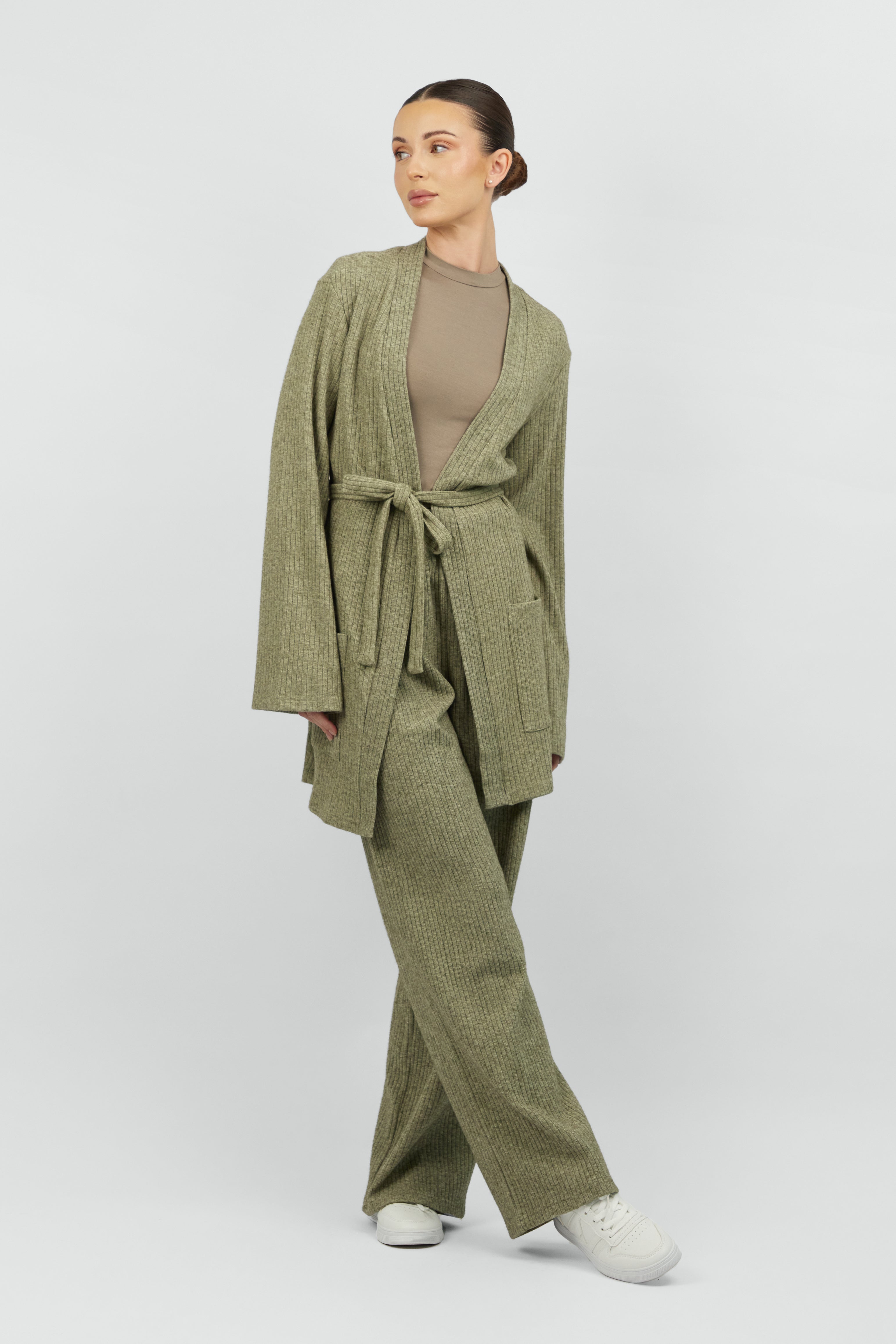 The girl wearing FARES' knit belted cardigan is looking to the right with her legs crossed. Colour description: Muted Green.