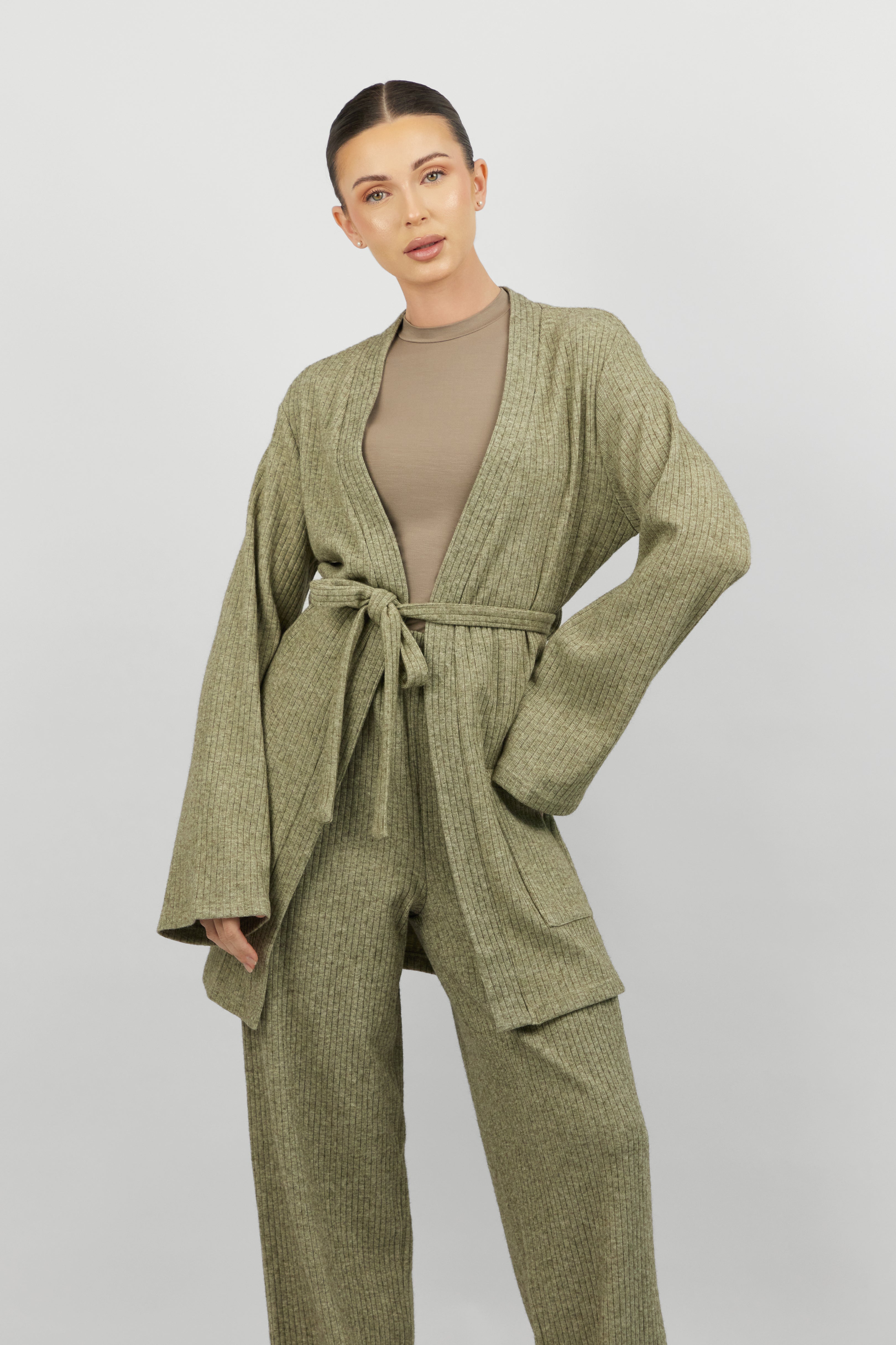 A close up of a model facing the camera wearing FARES' knit belted cardigan. Colour description: Muted Green.