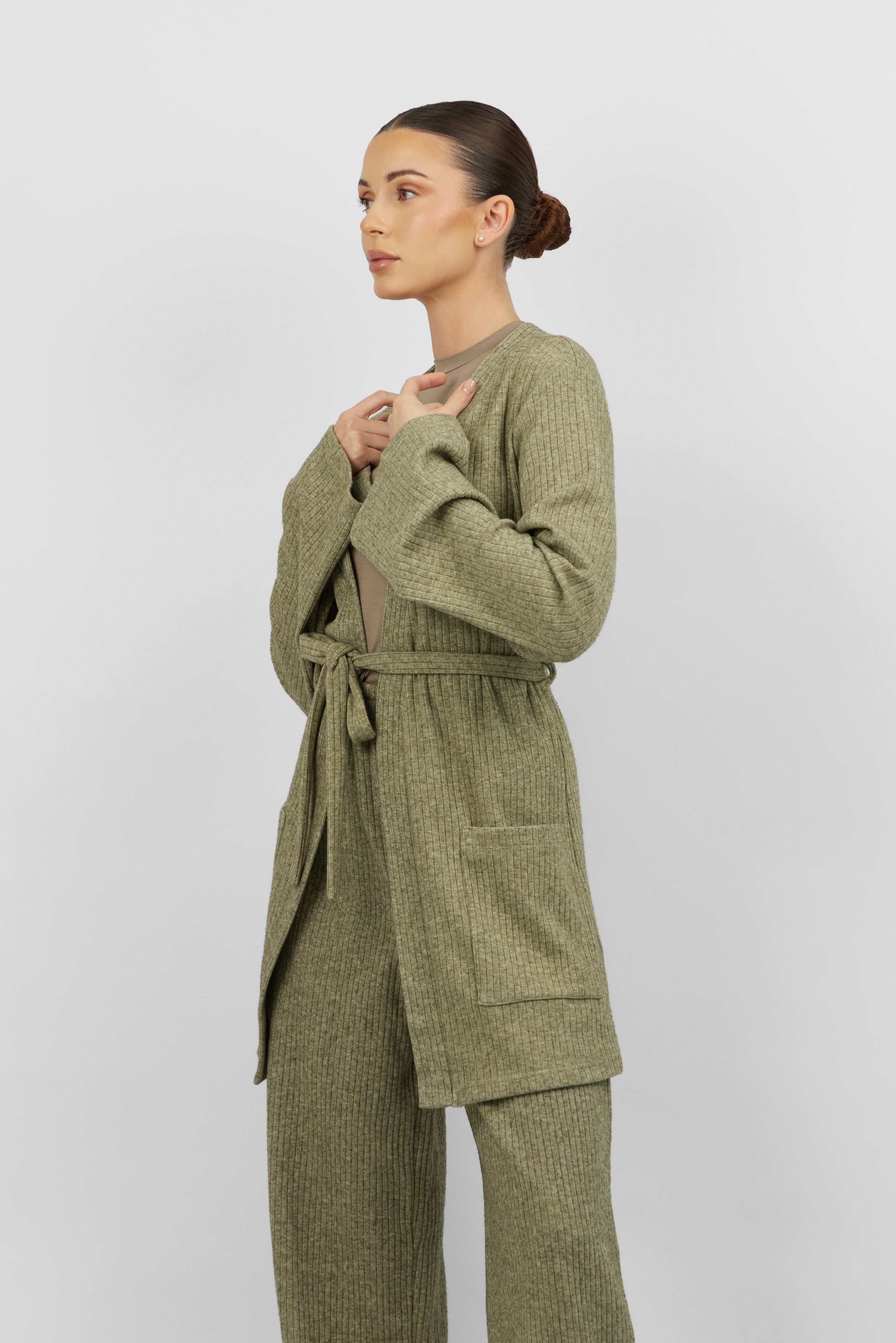 The girl wearing FARES' knit belted cardigan is turned to the right. Colour description: Muted Green.