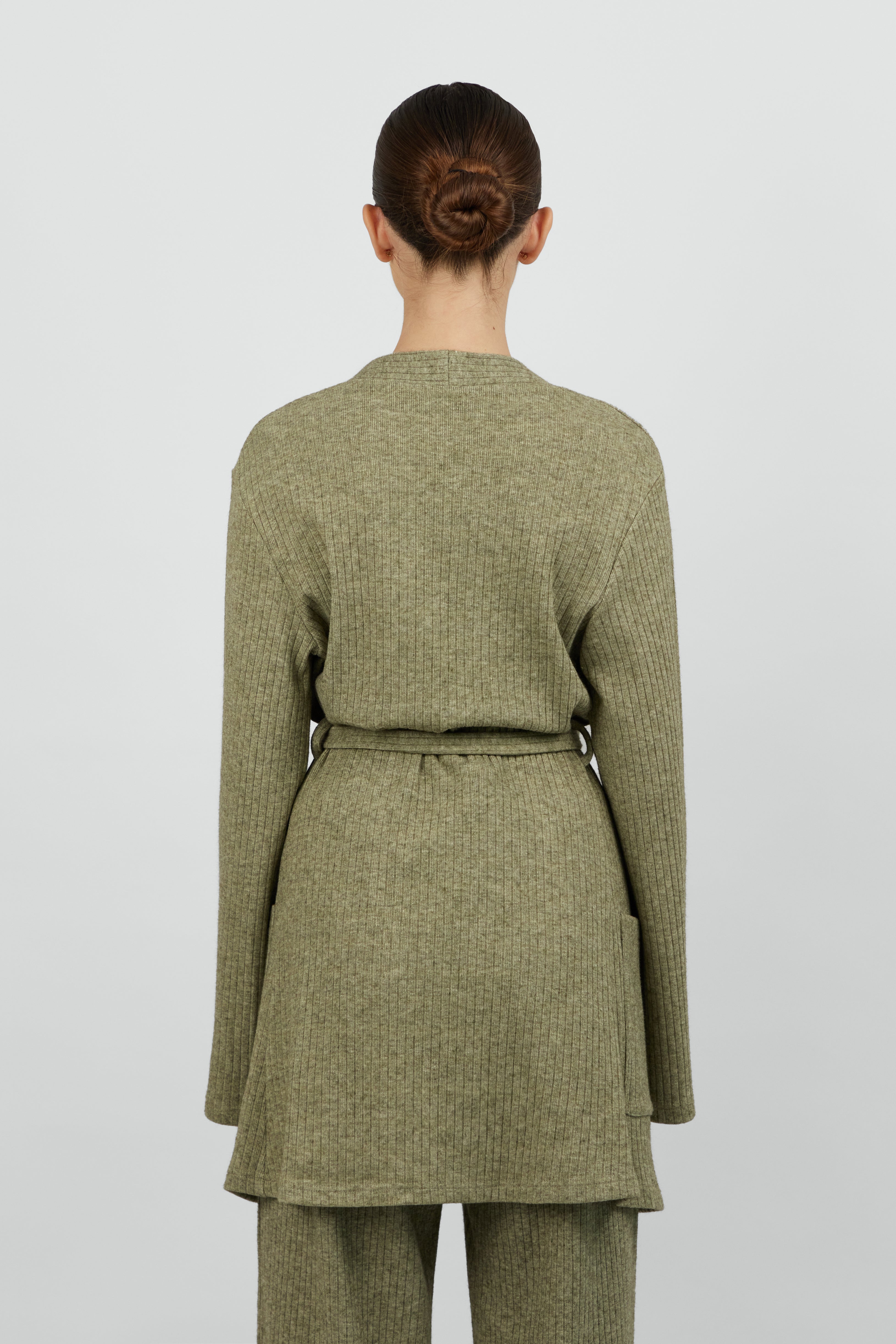 A girl is wearing FARES' knit belted cardigan and she is standing with her back to the camera. Colour description: Muted Green.