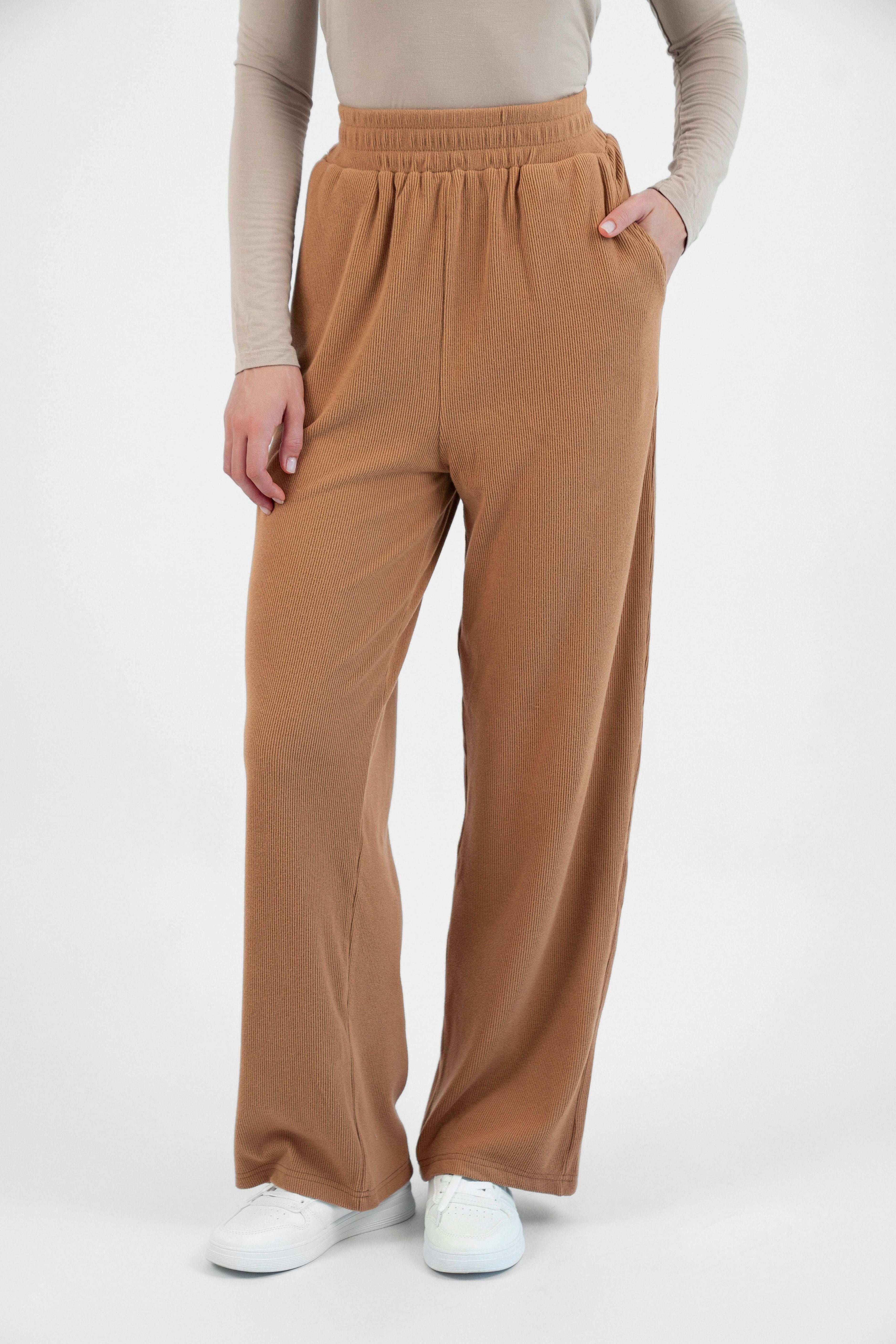 A model is wearing FARES' velour knit pants with her hand in her pocket. Colour description: Toffee.