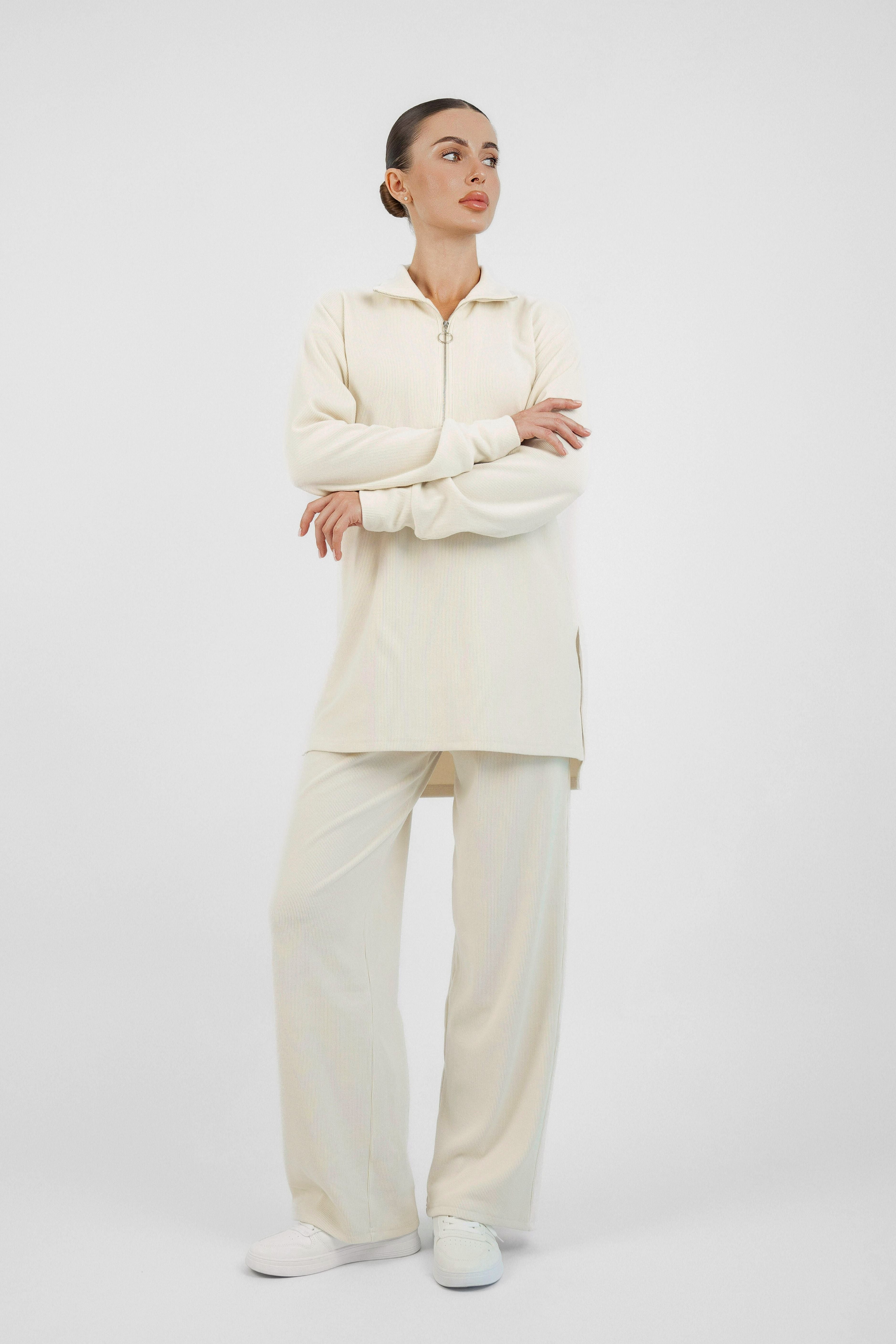 A girl is wearing FARES' velour knit half zip. Colour description: Creamy Page. Her hands are crossed front of her body.