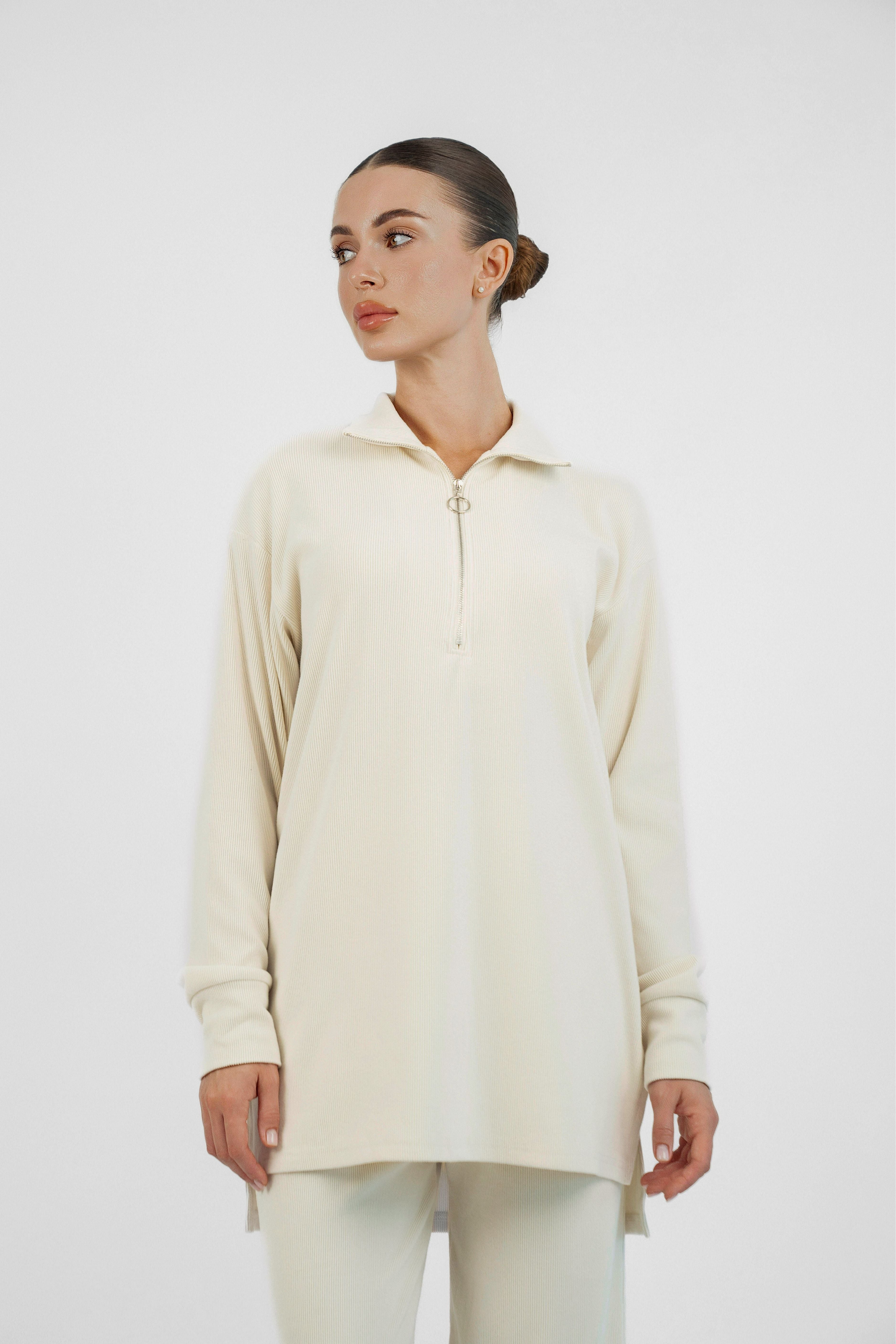 A model is wearing FARES' velour knit half zip with her head turned to the right. Colour description: Creamy Page.