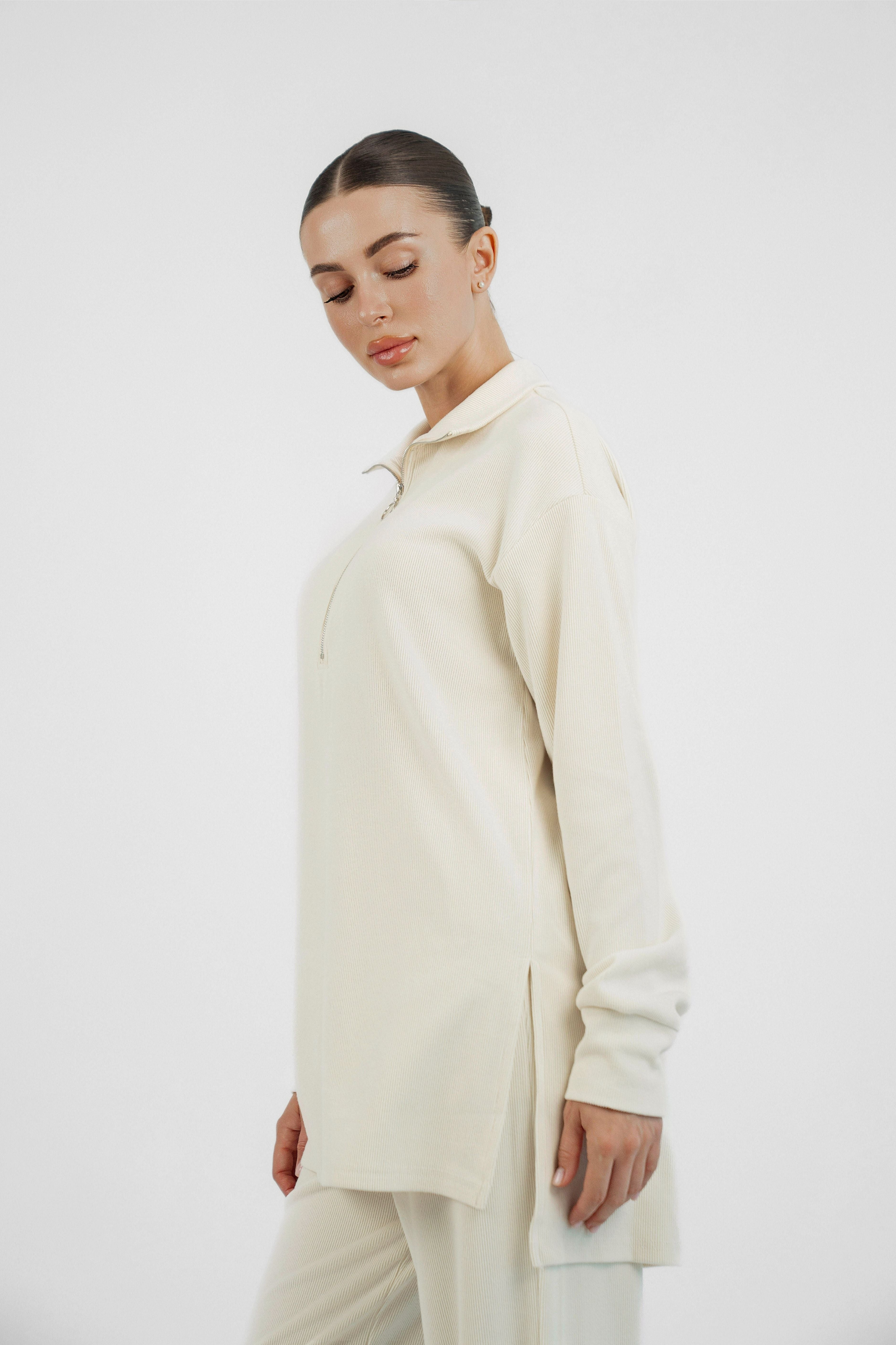 A model turned to the right and looking down wearing FARES' velour knit half zip. Colour description: Creamy Page.