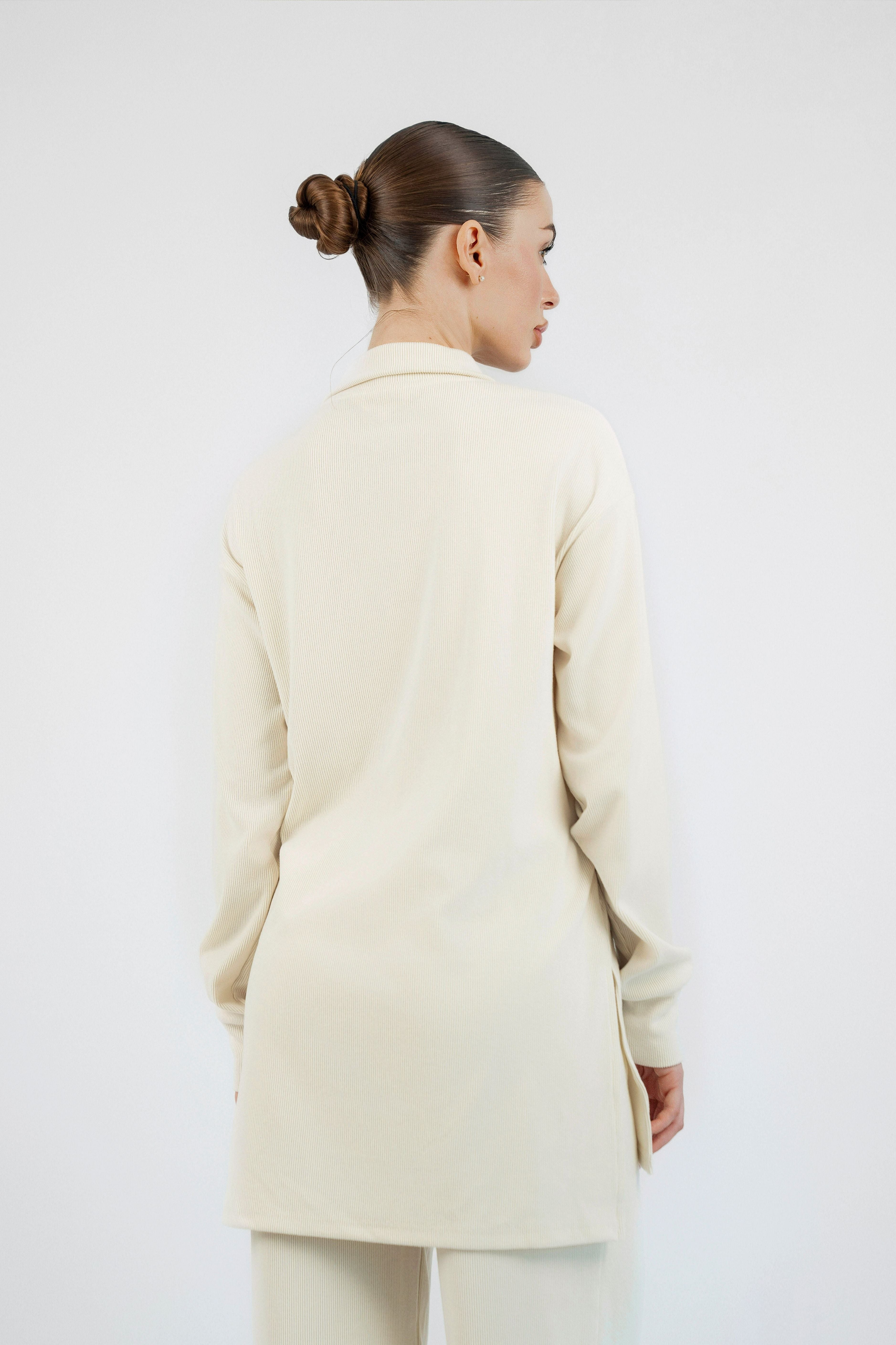 The model is standing with her back to the camera looking to the right. Colour description: Creamy Page. She is wearing FARES' velour knit half zip.