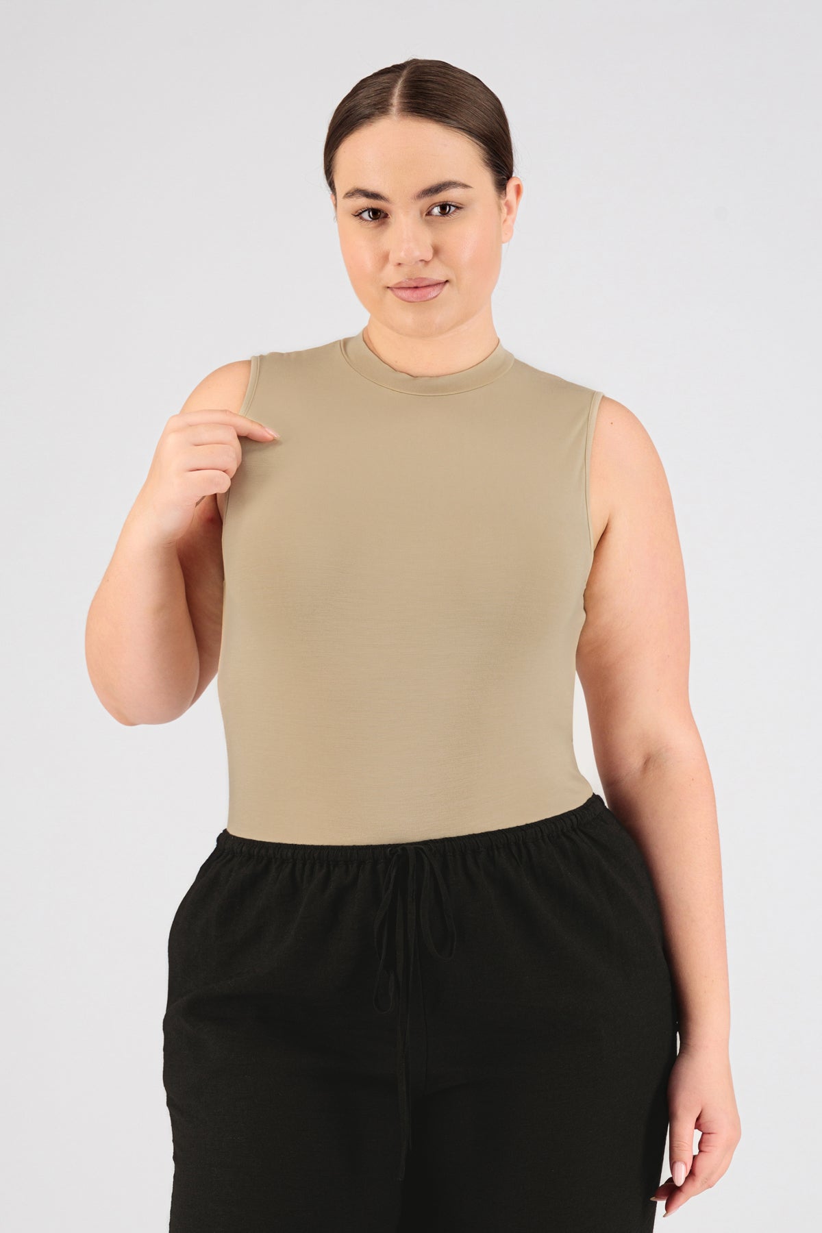 A girl is facing the camera while wearing FARES' sleeveless layer. Colour description: Buff. Her right hand is lifted to her shoulder.
