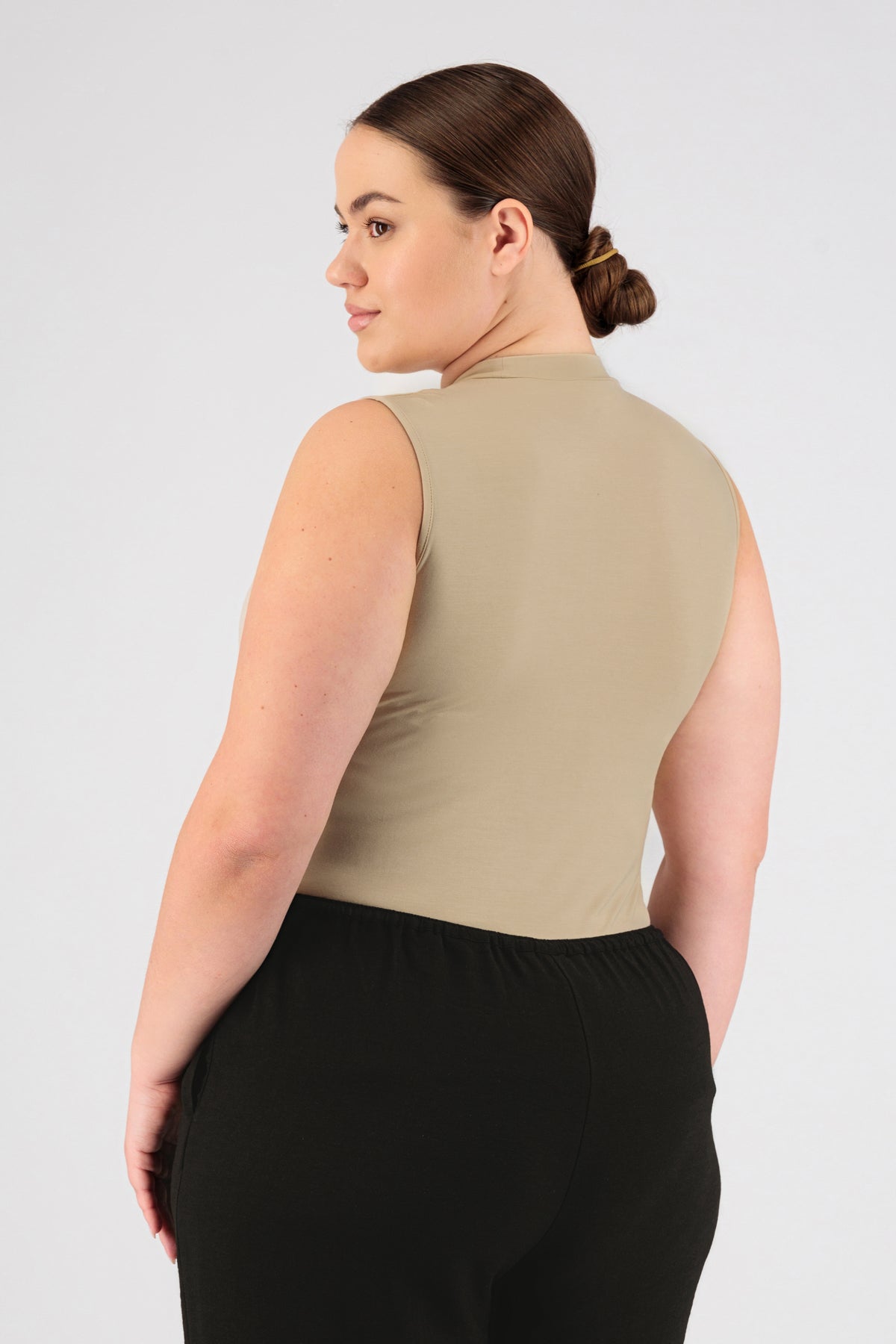 A girl wearing FARES' sleeveless layer is shown from the back while looking over her left shoulder. Colour description: Buff.