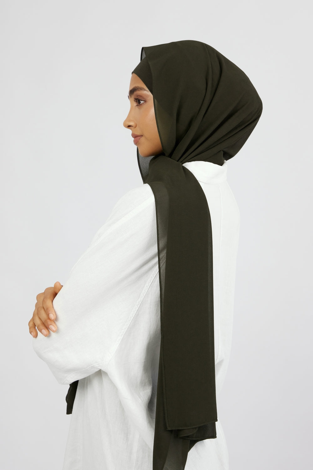 A woman wearing one of FARES's matching chiffon hijab sets. The model is turned to the left. Colour description: dark green.
