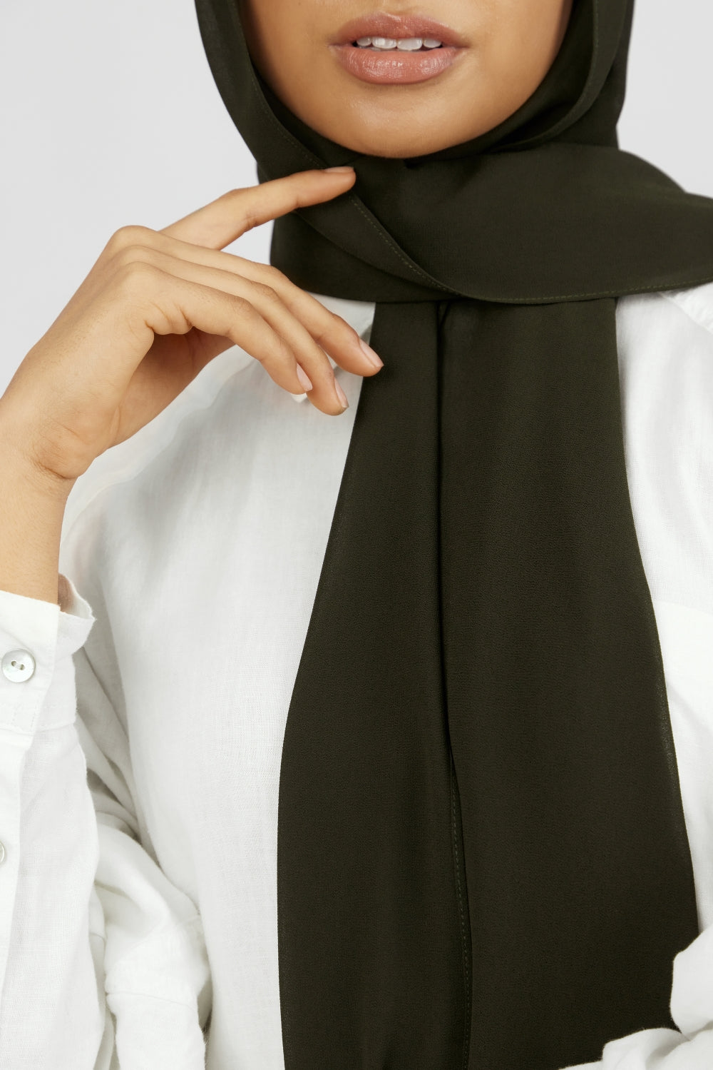 A close-up of a woman wearing FARES's matching chiffon hijab set. Colour description: dark green.