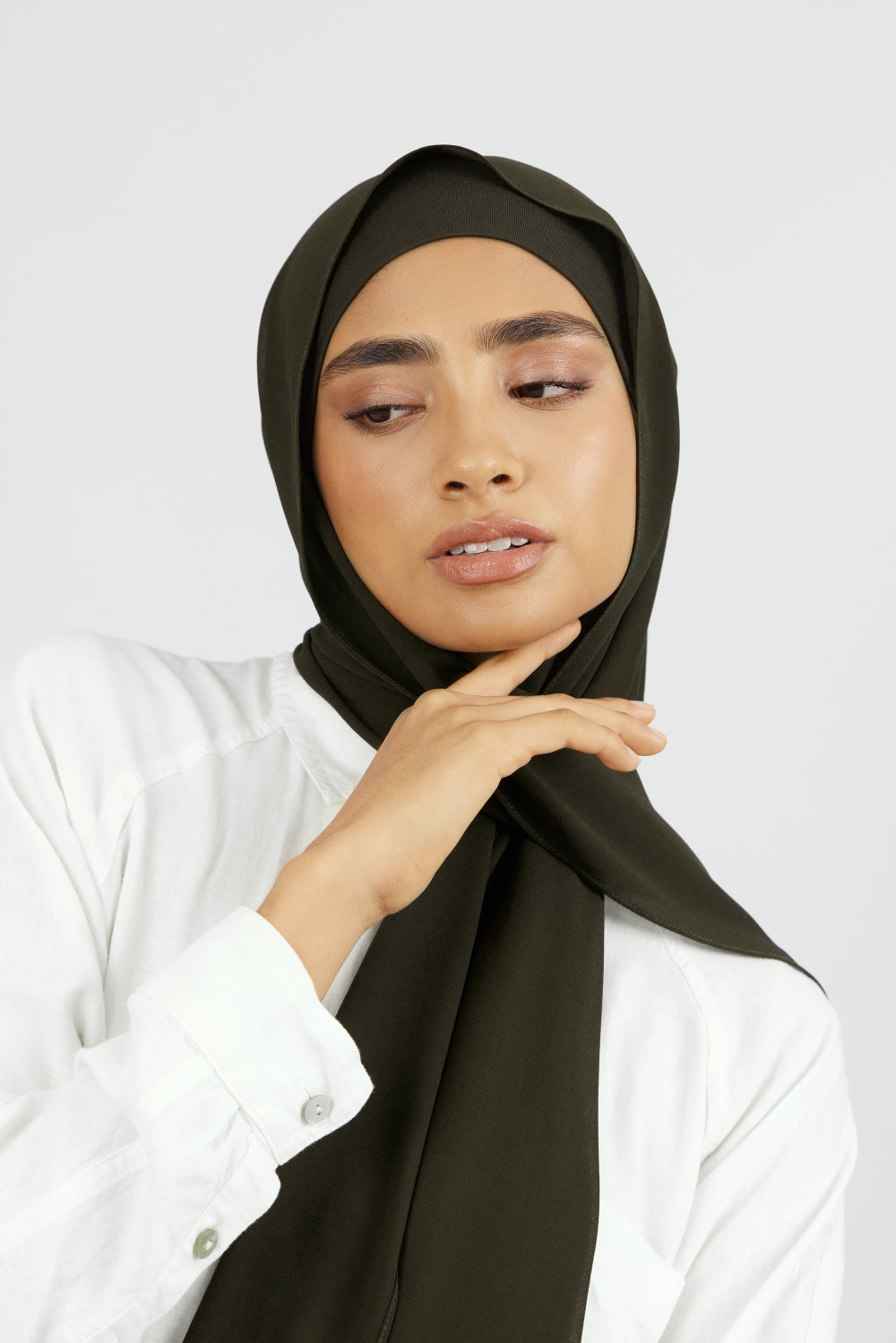 The front of a woman touching the matching chiffon hijab set she wears. Colour description: dark green.