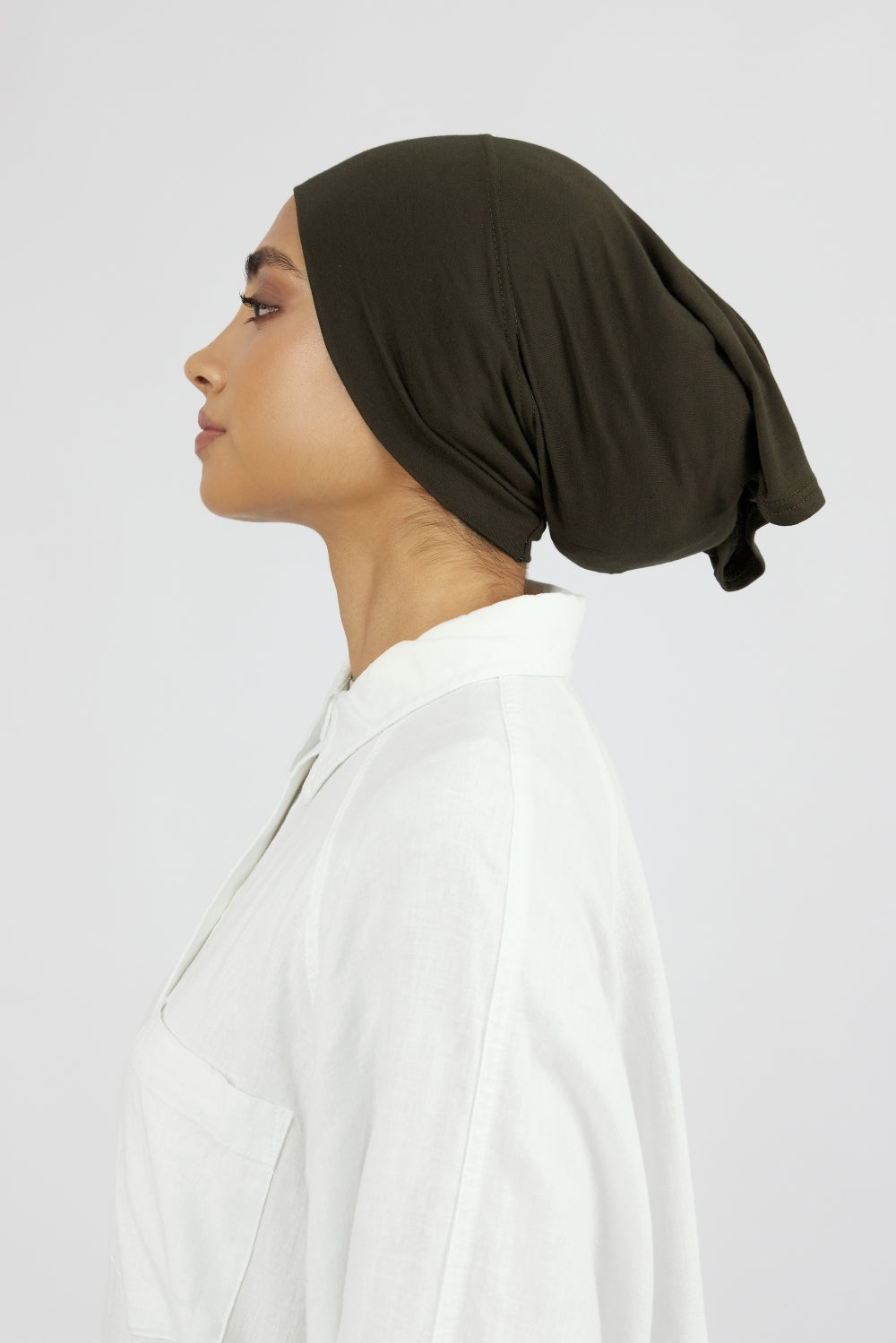 The left profile of a woman wearing a breathable hijab undercap. Colour description: dark green.