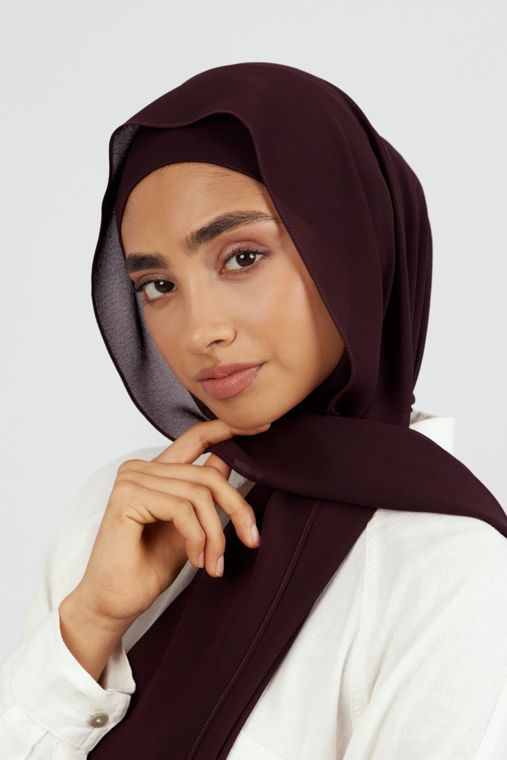 A woman wearing one of FARES's matching chiffon hijab sets. The model is turned to the left. Colour description: deep plum.