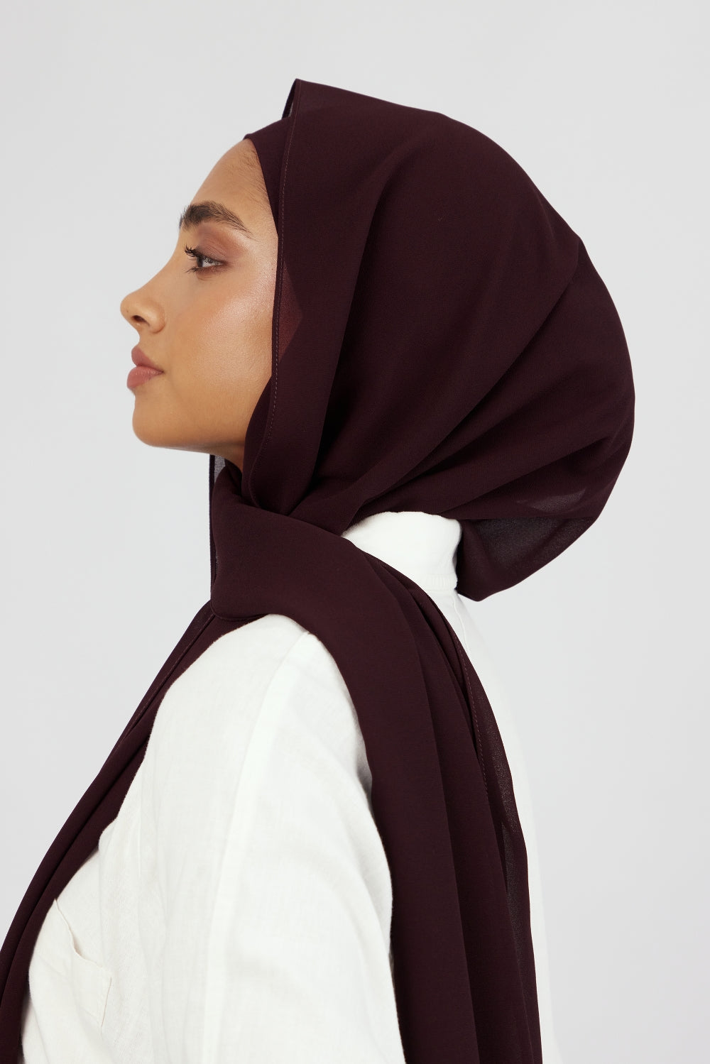 The left profile of a woman wearing one of FARES's matching chiffon hijab sets. Colour description: deep plum.