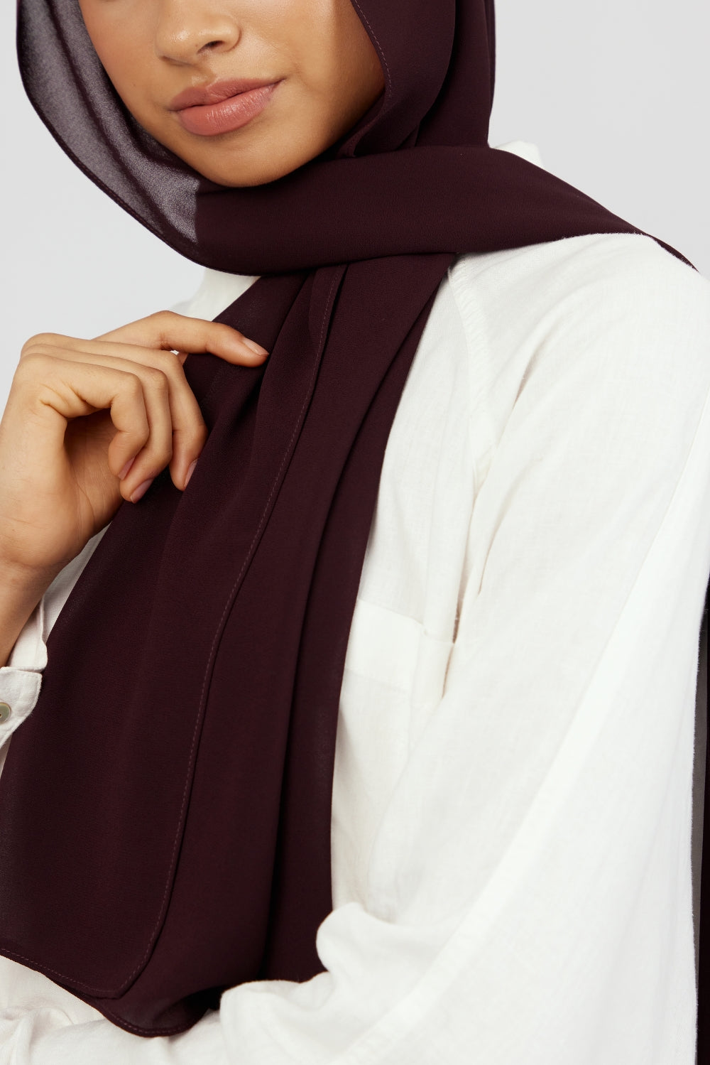 A close-up of a woman wearing a matching chiffon hijab set. from FARES. The model is turned to the left. Colour description: deep plum.