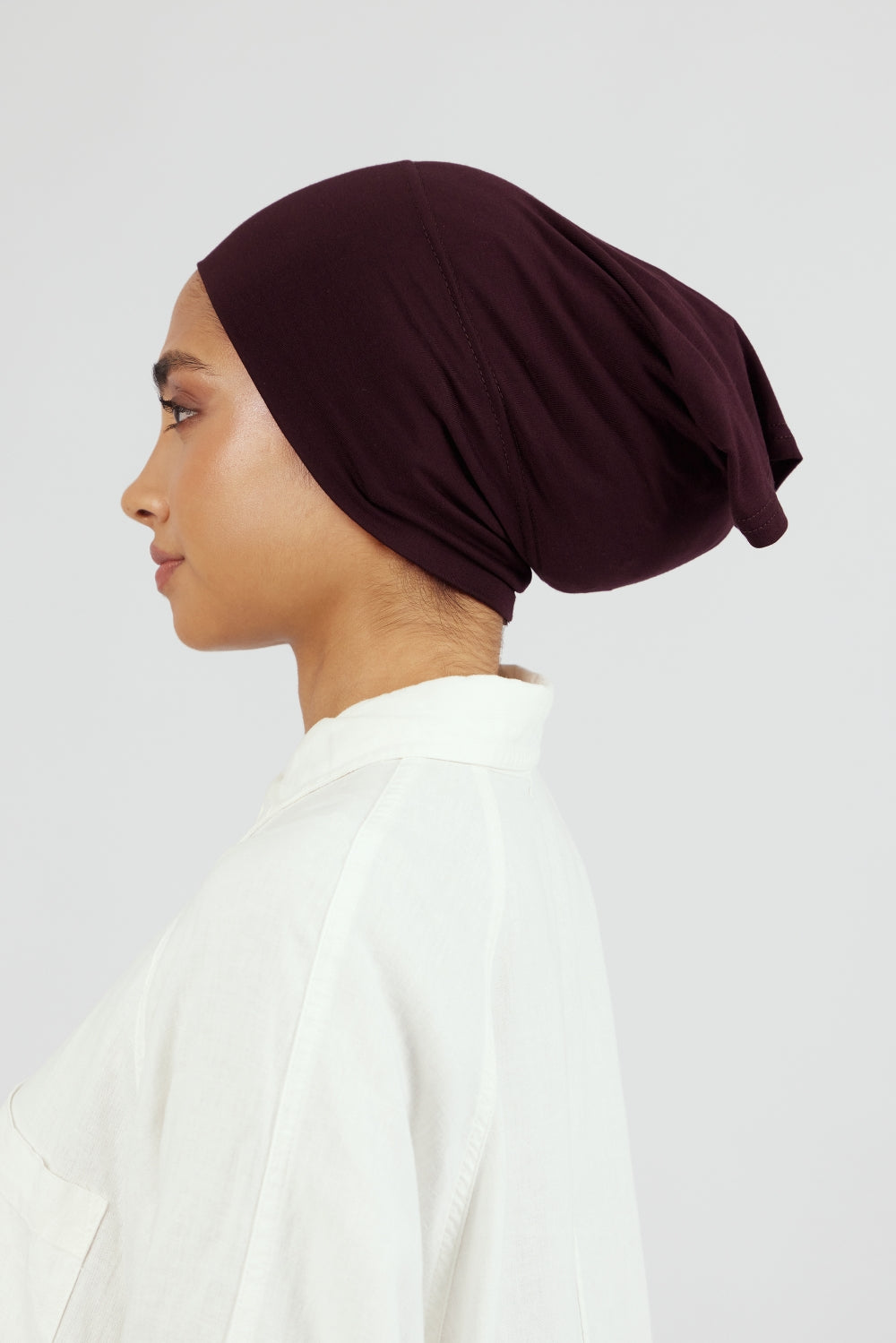 The left profile of a woman wearing a breathable hijab undercap. Colour description: deep plum.