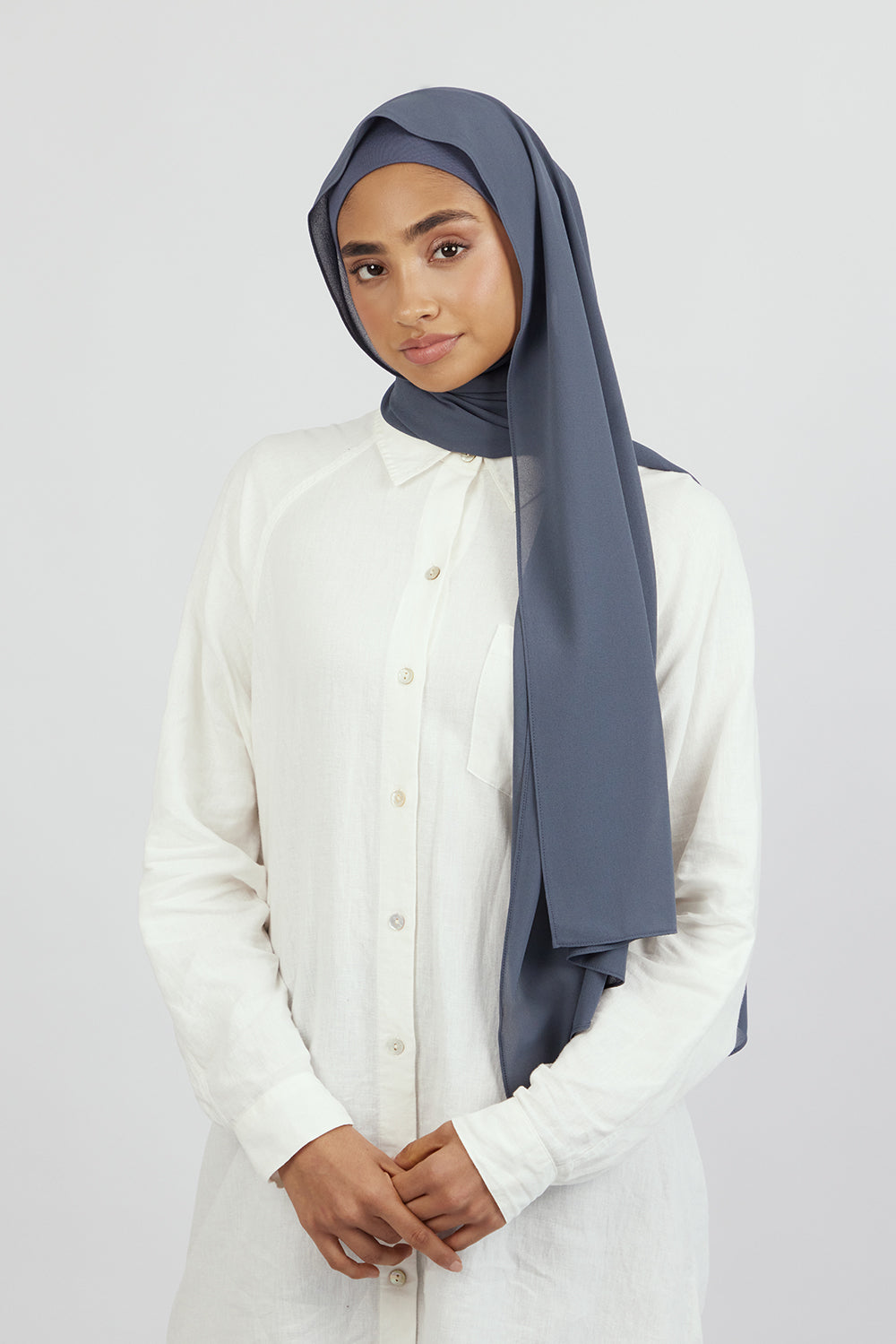 The front of a female model wearing a matching chiffon hijab set. This hijab fashion wear includes a high quality chiffon hijab and a breathable matching modal jersey undercap. Colour description: denim blue.