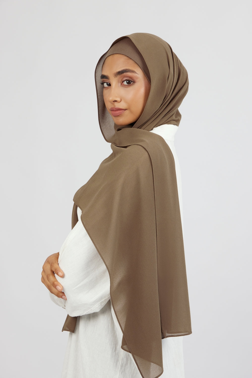 A female model wearing a matching chiffon hijab set. The model is standing side ways and looking over her left shoulder. Colour description: medium beige-brown.