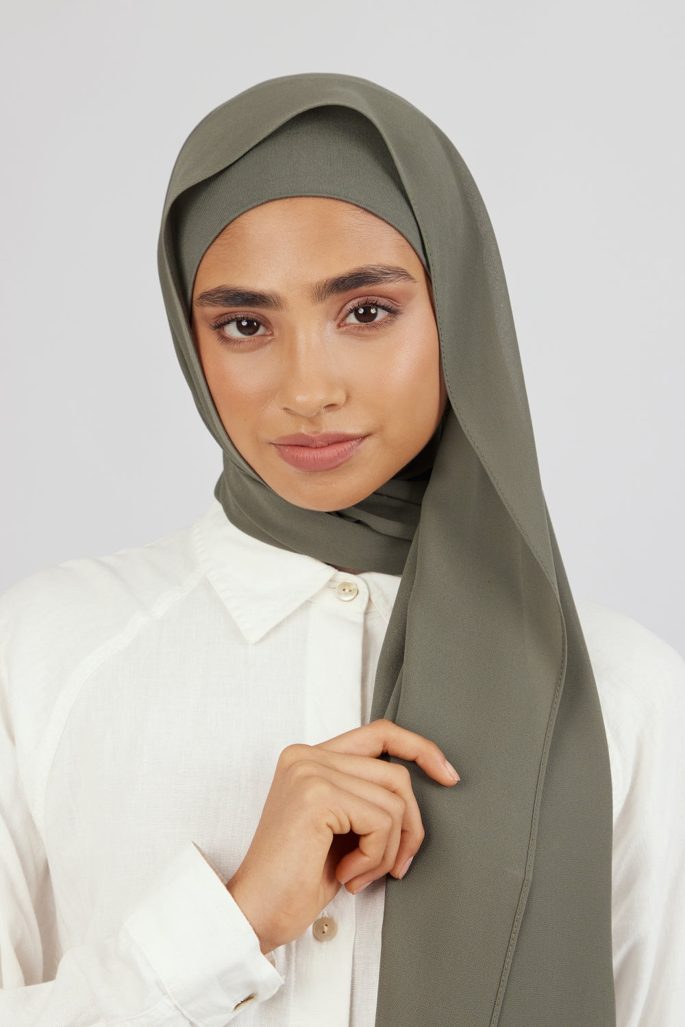 The front of a woman touching the matching chiffon hijab set she wears. Colour description: muted green.