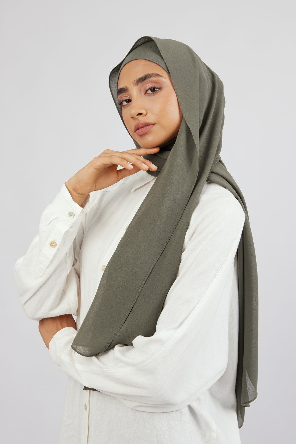 A woman touching the matching chiffon hijab set from FARES she wears. Colour description: muted green.
