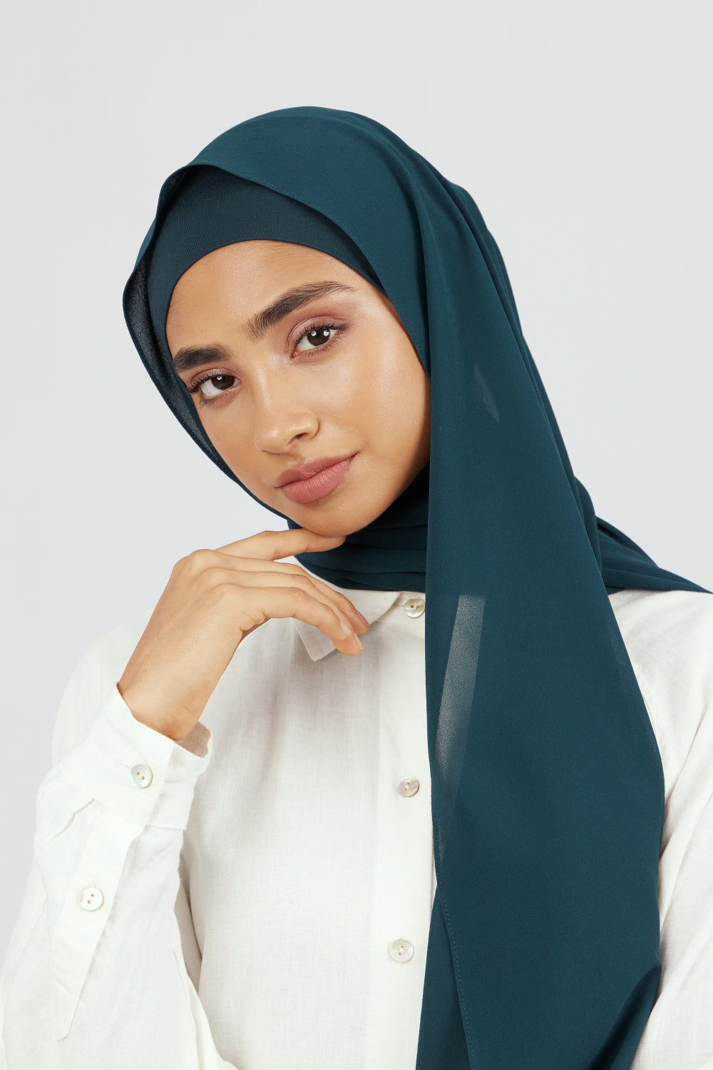 The front of a woman touching the matching chiffon hijab set she wears. Colour description: dark teal.