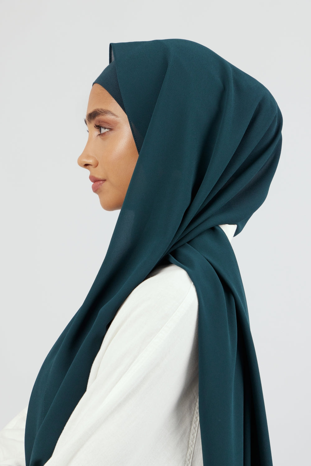 A woman wearing one of FARES's matching chiffon hijab sets. The model is turned to the left. Colour description: dark teal.