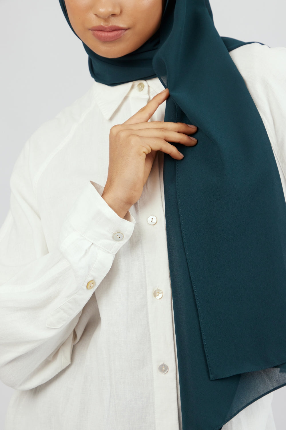 A close-up of a woman wearing a matching chiffon hijab set. Colour description: dark teal.