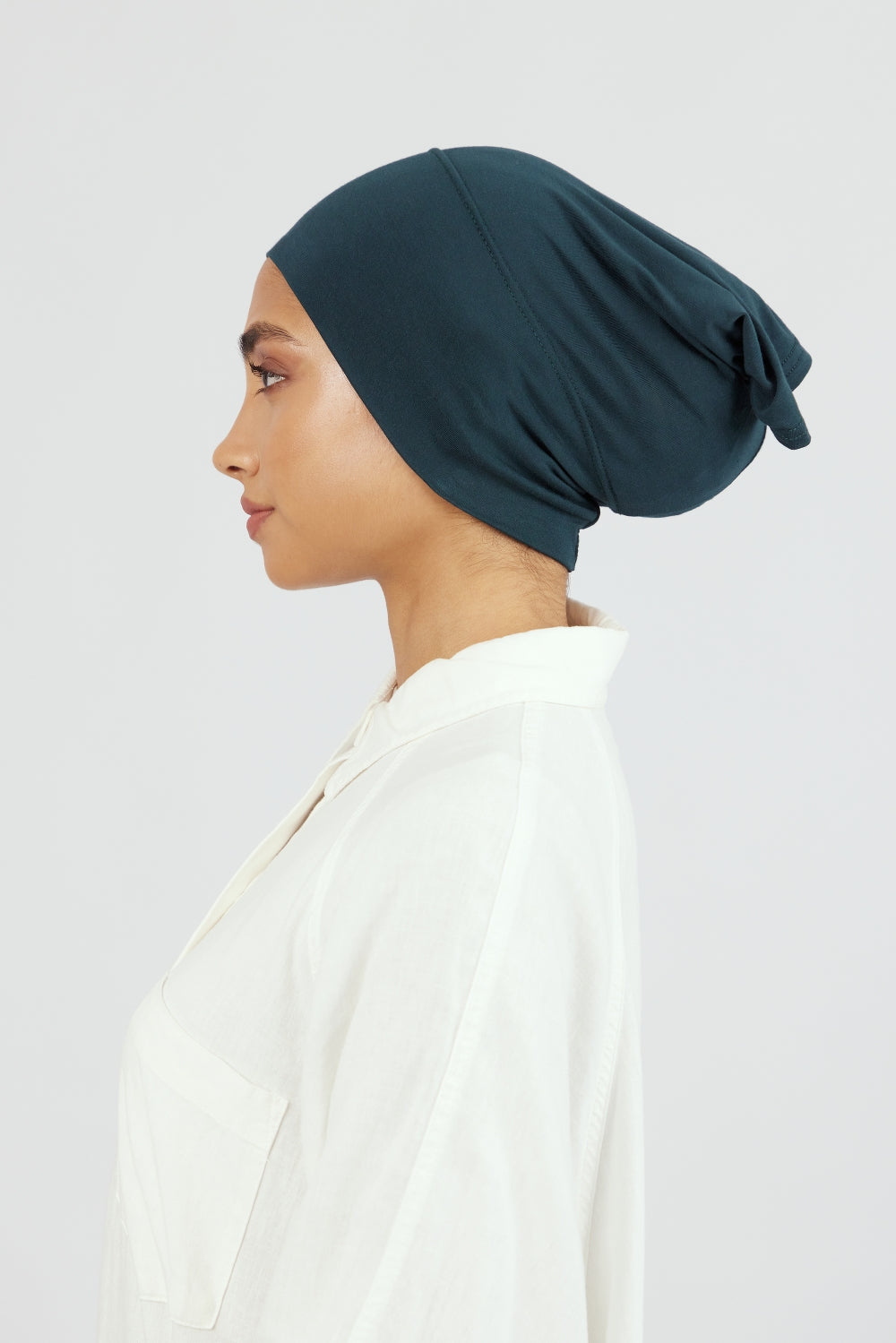 The left profile of a woman wearing a breathable hijab undercap. Colour description: dark teal.