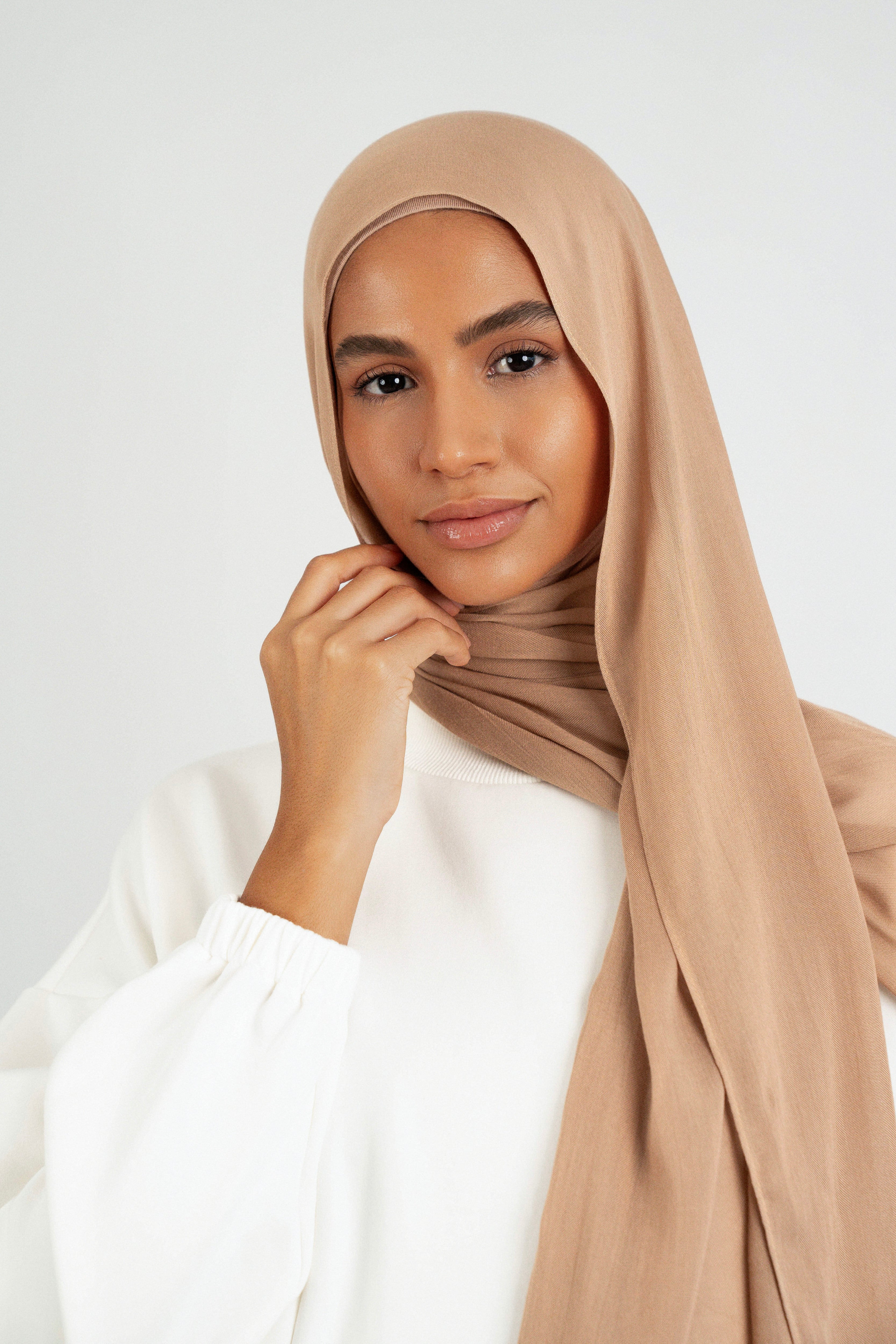 A close up of girl wearing a Matching Butter Modal Hijab Set and touching her face. Colour: Almond