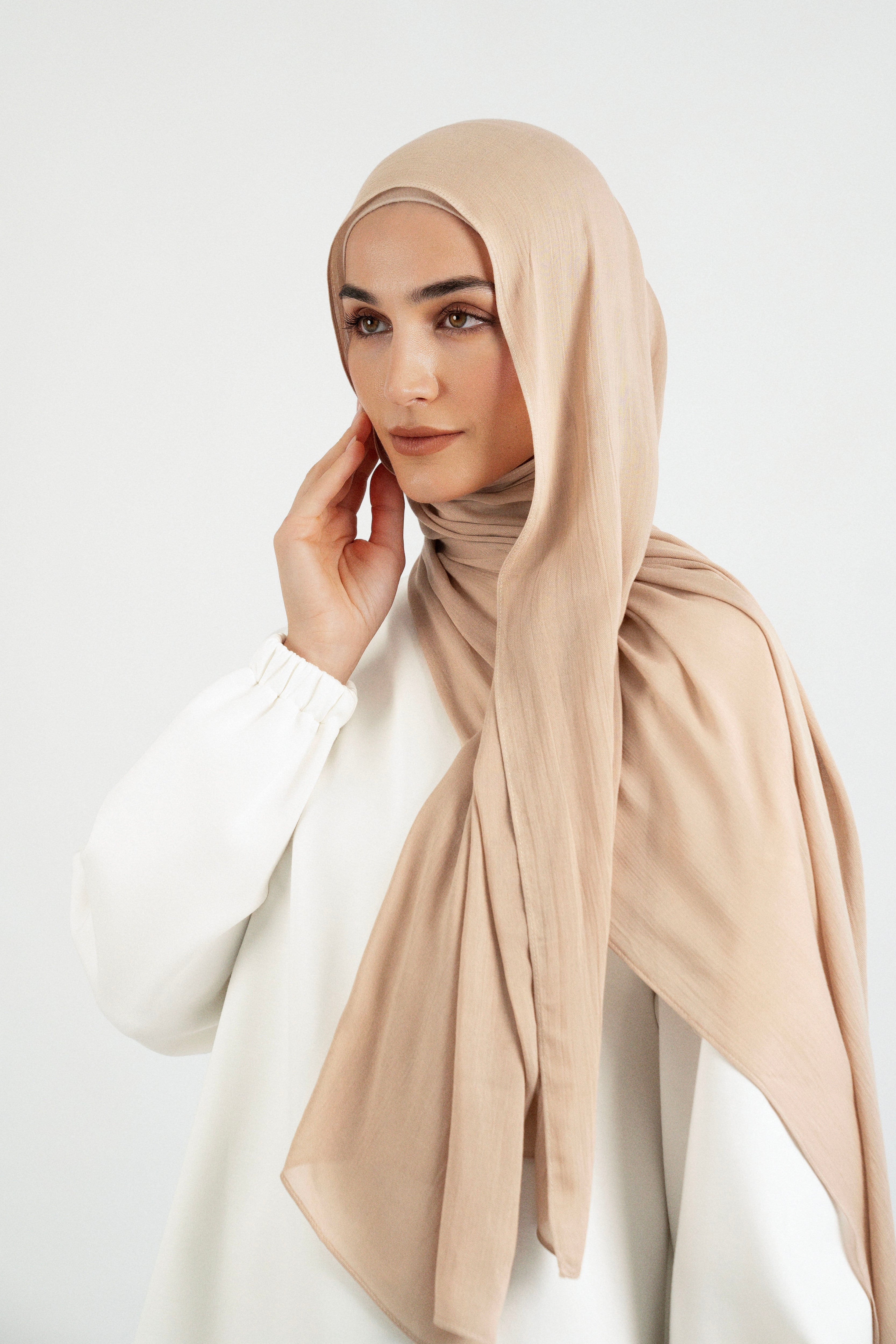 Colour: Biscuit. A model is wearing a Matching Butter Modal Hijab Set and touching her face.